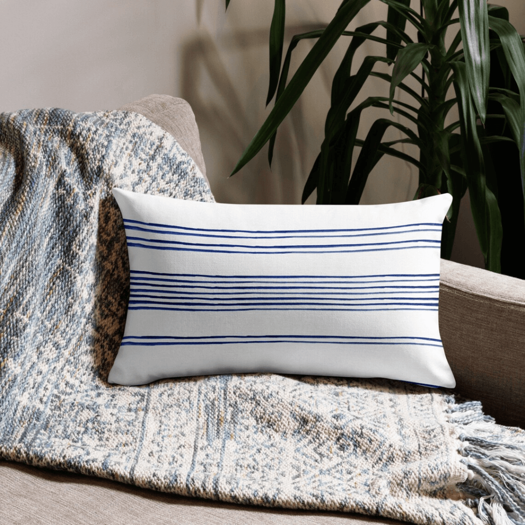 Hamptons Striped Pillow on a cozy couch with a blanket, featuring blue and white stripes for coastal decor.