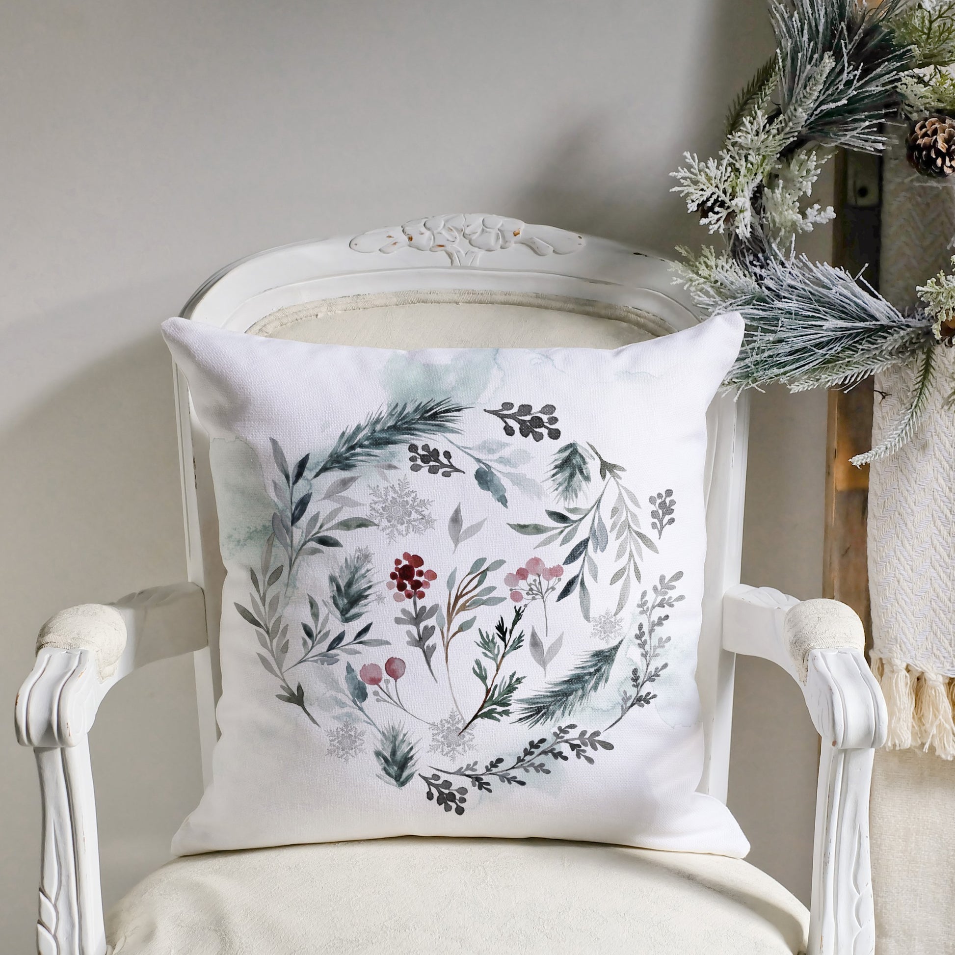 Winter botanical pillow with watercolor wreath on white chair and holiday greenery – cozy seasonal decor