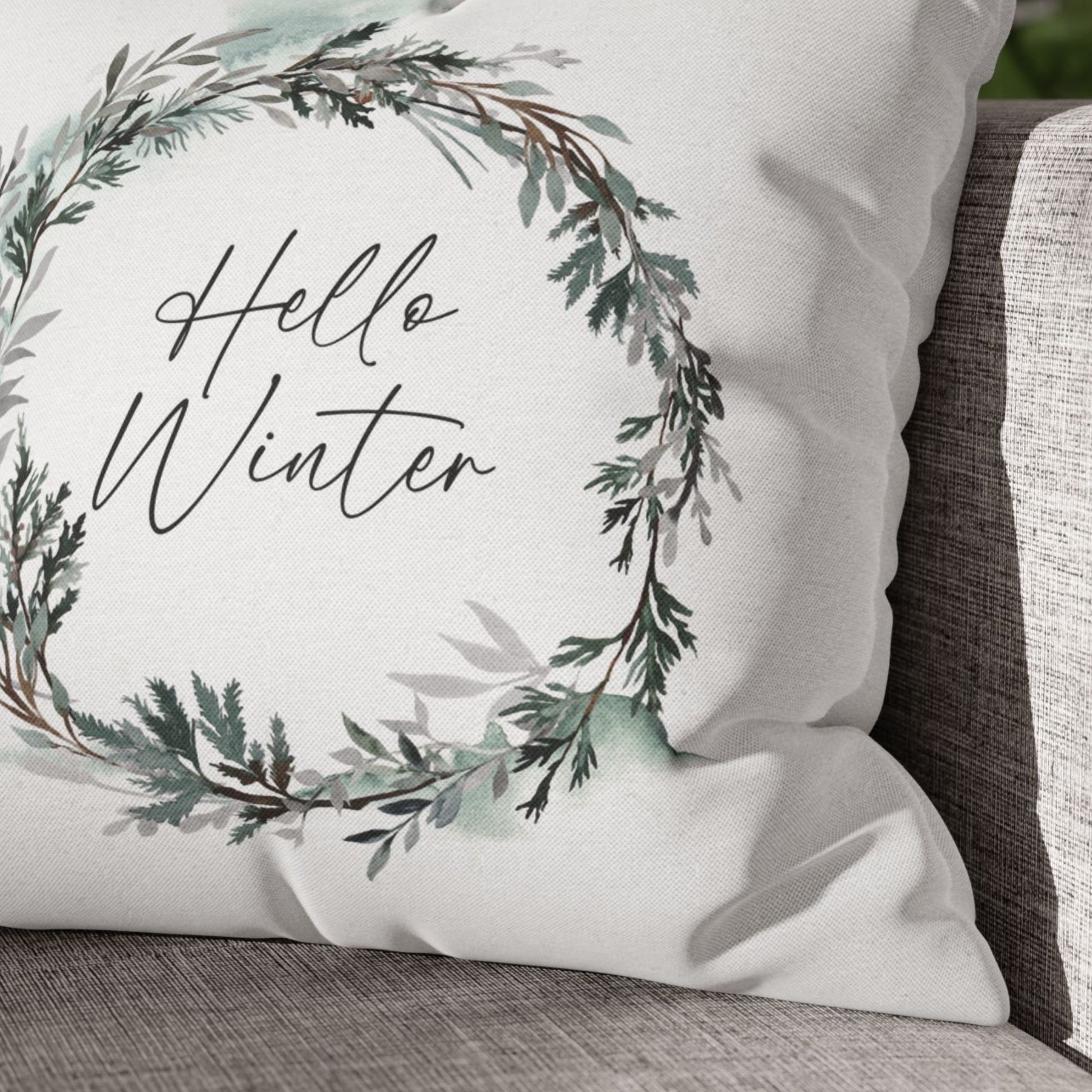 Hello Winter pillow close-up with botanical wreath design on neutral sofa – cozy Christmas decor