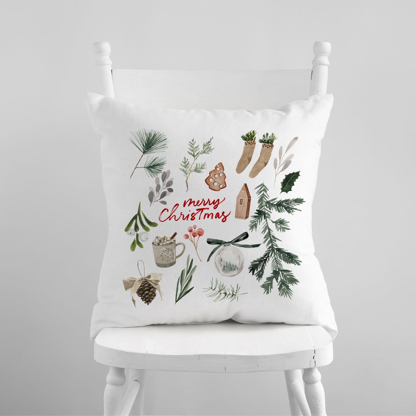 White pillow with watercolor holiday illustrations and red Merry Christmas text on white chair – festive winter decor