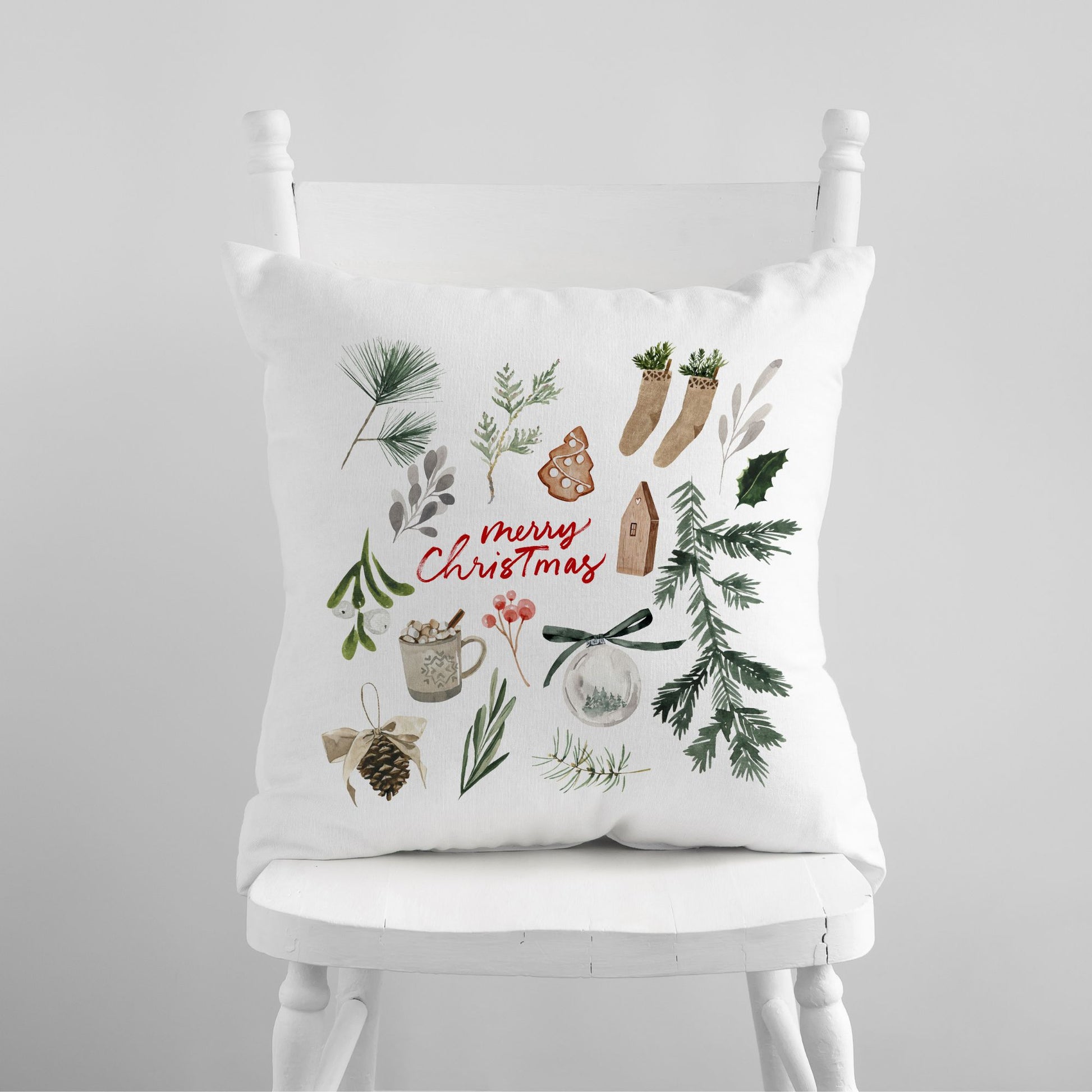White pillow with watercolor holiday illustrations and red Merry Christmas text on white chair – festive winter decor