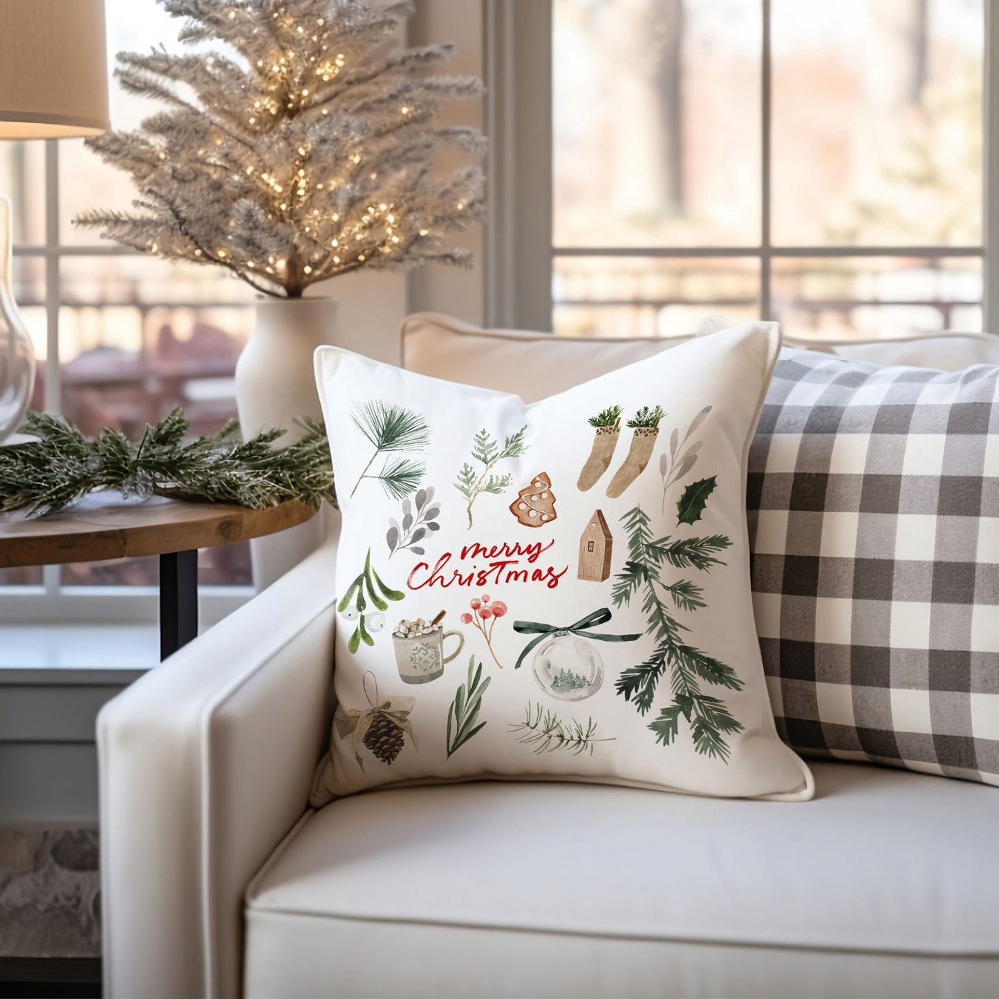 Merry Christmas watercolor pillow styled on white armchair with holiday tree, garland, and checkered cushion