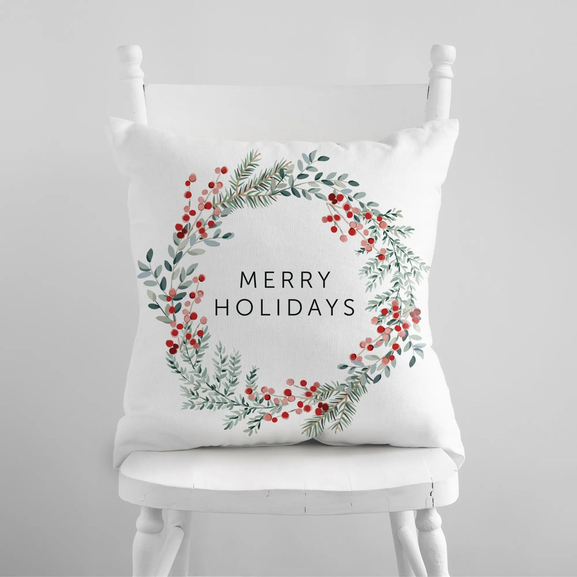 Merry Holiday Christmas wreath pillow with watercolor pine and red berries on white chair – festive seasonal decor