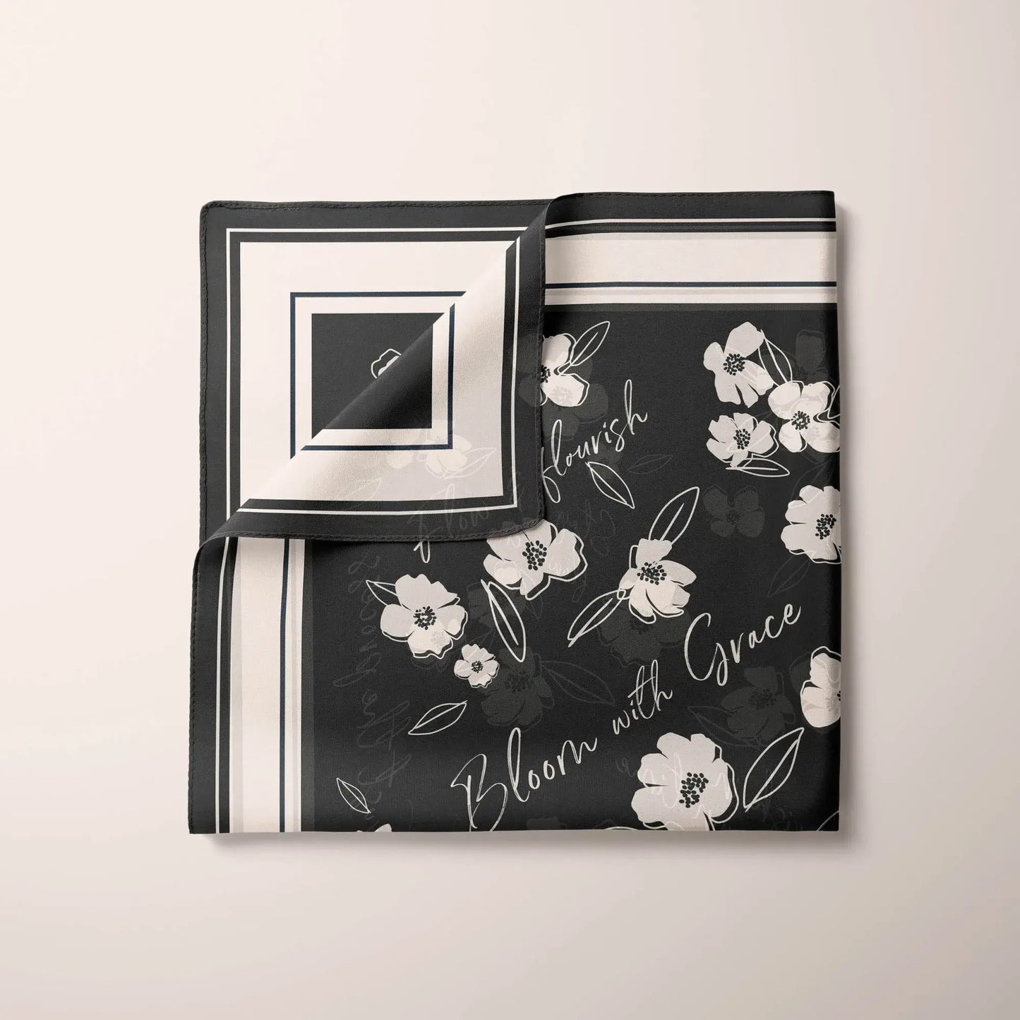 Partially folded black silk scarf showing white wildflower details and the inspirational messages "flourish" and "Bloom with Grace".