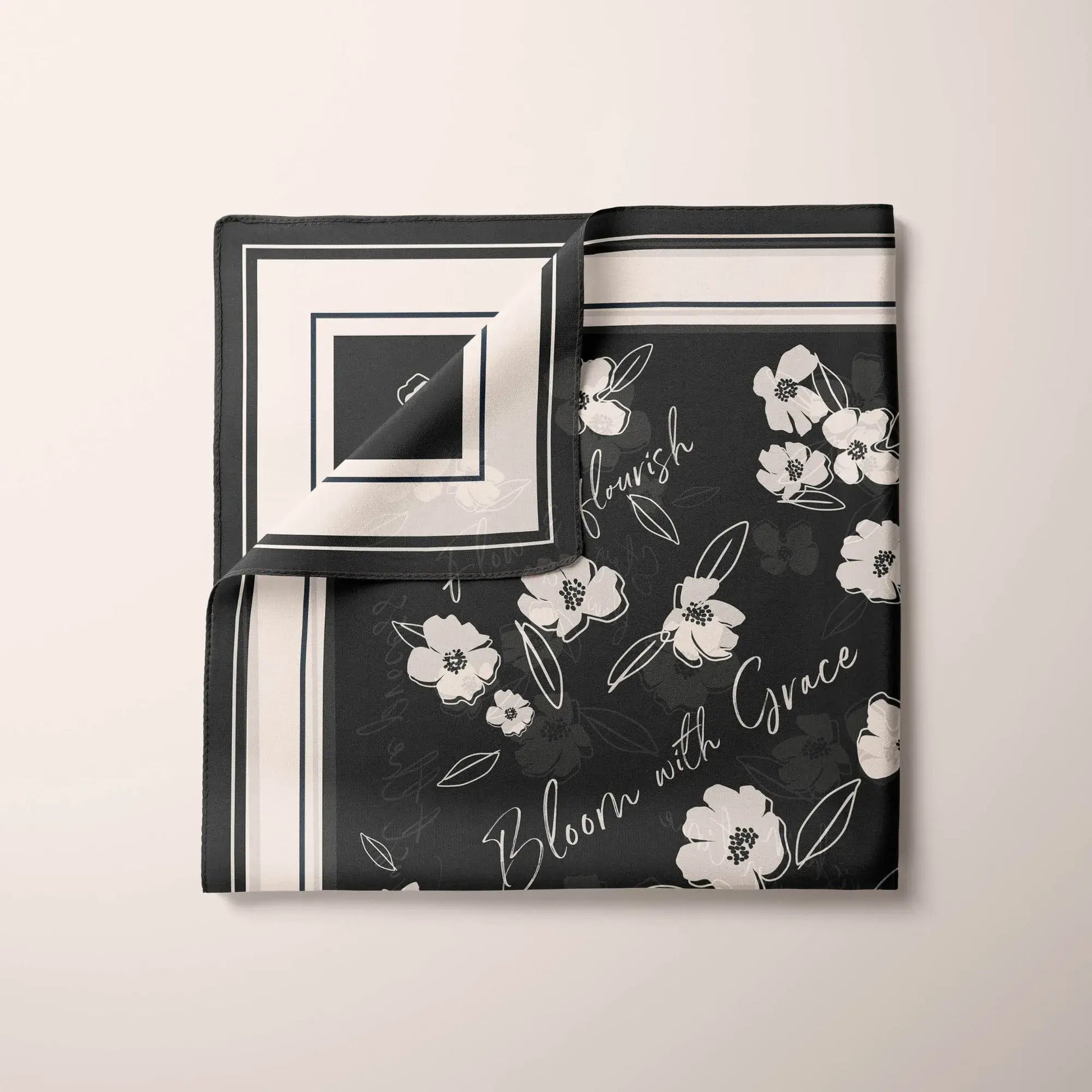 Partially folded black silk scarf showing white wildflower details and the inspirational messages "flourish" and "Bloom with Grace".