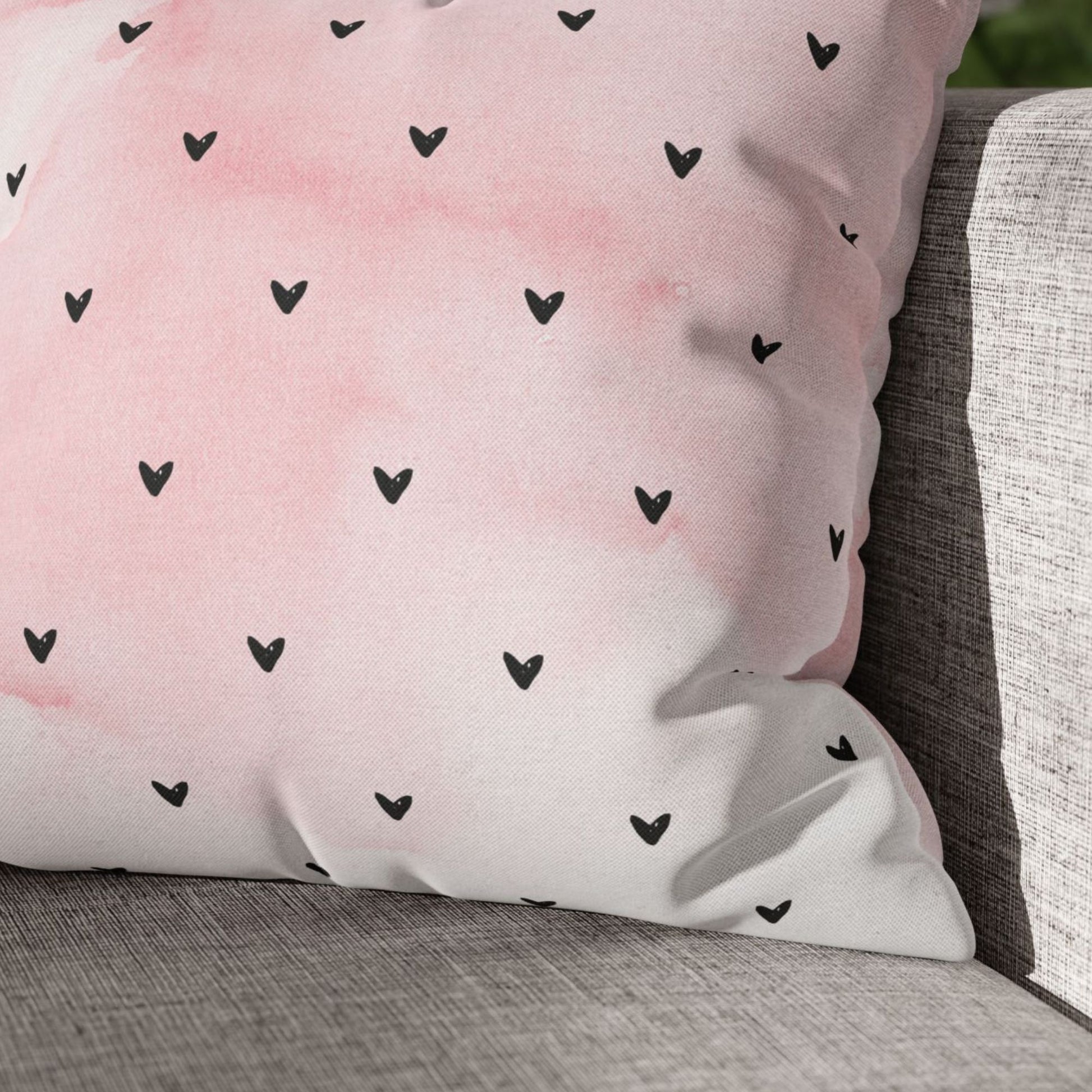 Close-up of a pink Minimalist Hearts Valentine Pillow with black hearts, resting on a gray textured sofa, Blue Water Songs brand.