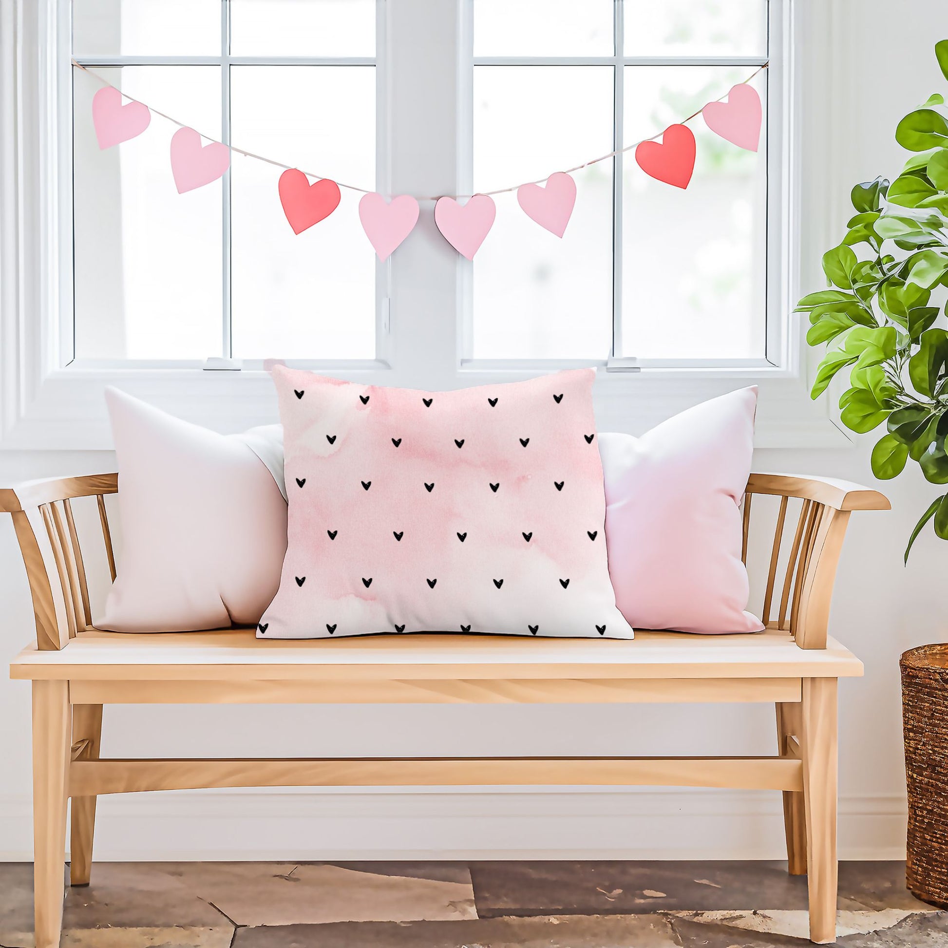 Minimalist Hearts Valentine Pillow by Blue Water Songs on a wooden bench with pink accent pillows. Heart garland decorates the window behind.