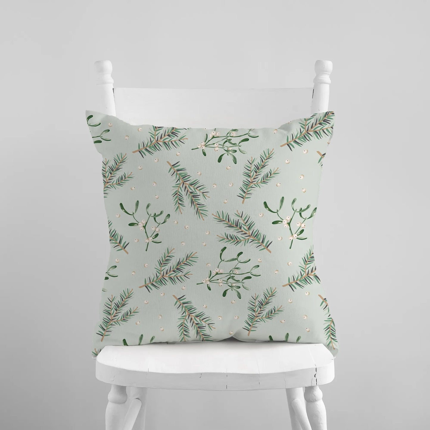 Mistletoe and pine branch Christmas pillow on white chair – botanical holiday cushion in soft green tones