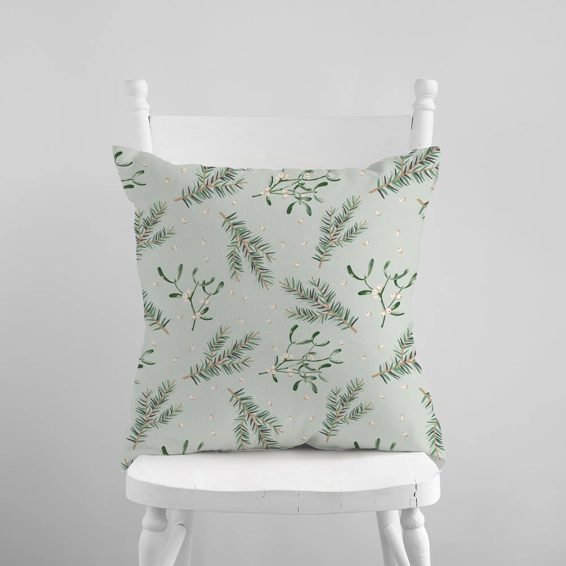 Mistletoe and pine branch Christmas pillow on white chair – botanical holiday cushion in soft green tones