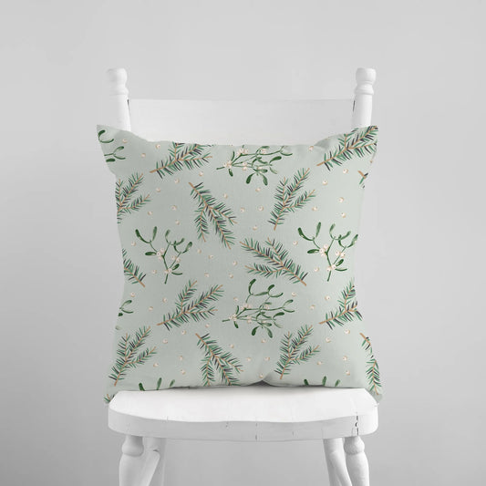 Mistletoe and pine branch Christmas pillow on white chair – botanical holiday cushion in soft green tones