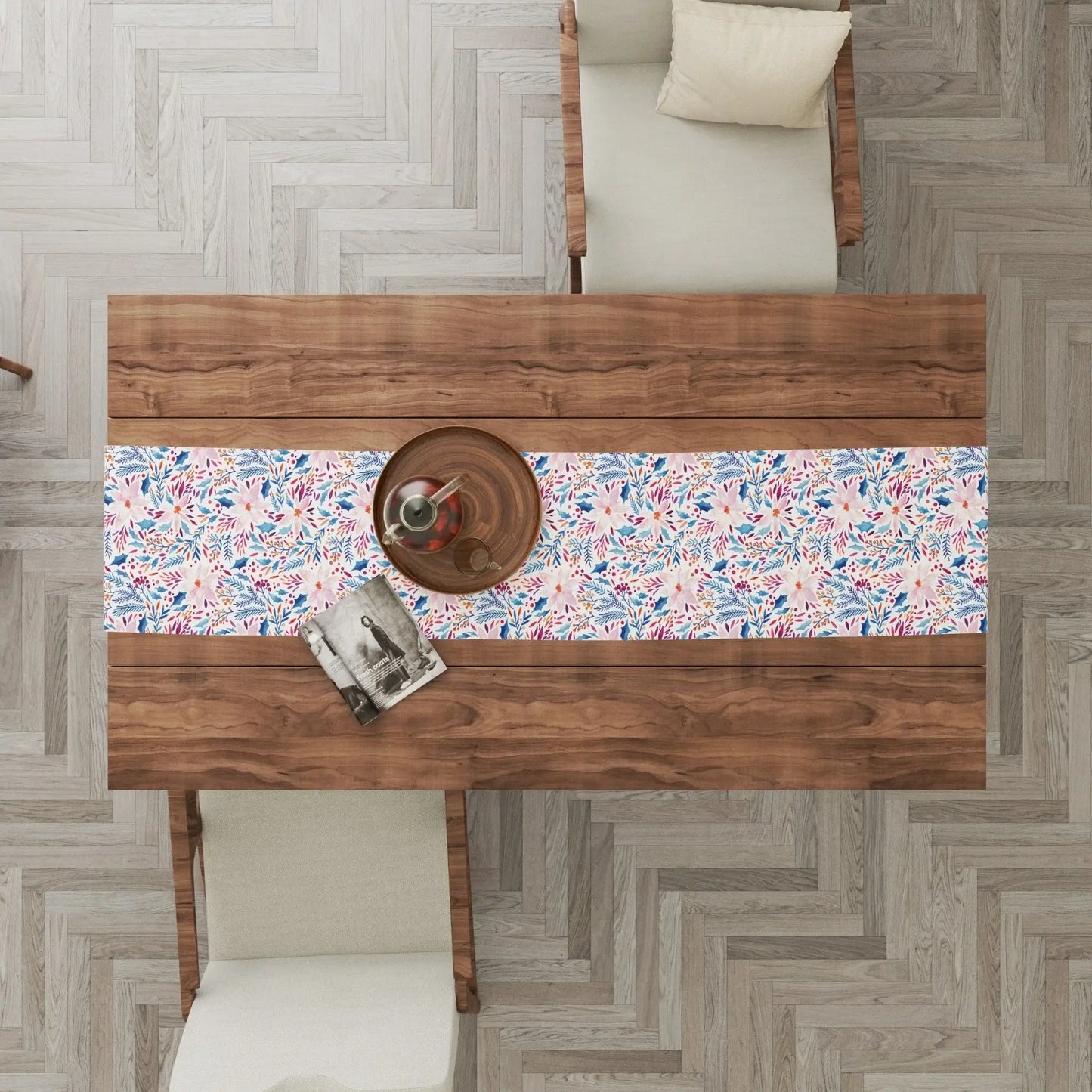 Top view of a wood dining table featuring a Pink Poinsettia Winter Table Runner with floral patterns and neutral chairs.