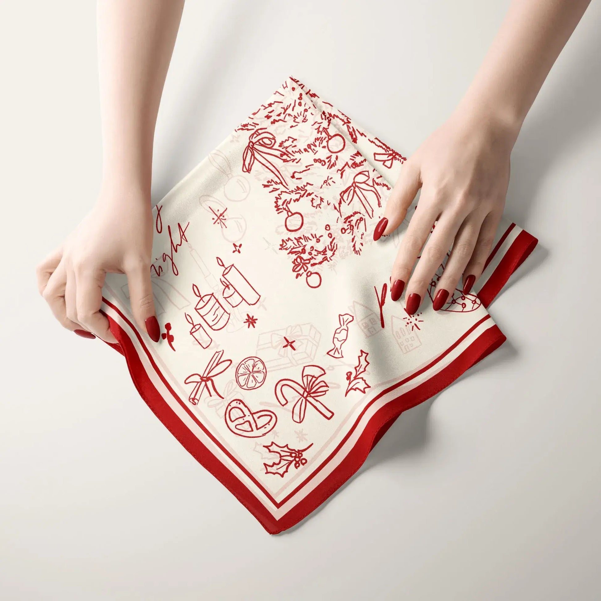 Hands folding red and ivory Christmas Silk Scarf “Make a Wish” with festive hand-drawn holiday illustrations.