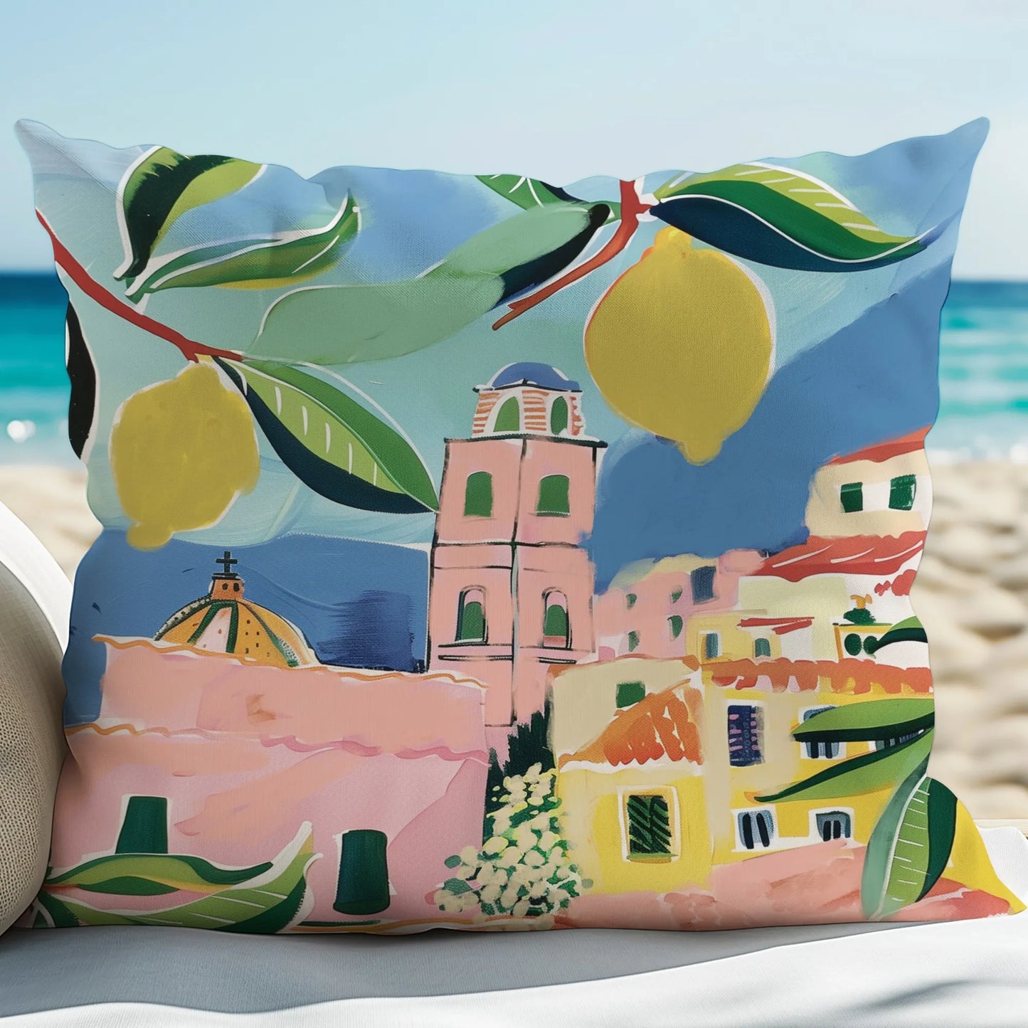 Colorful outdoor pillow with lemon and coastal town illustration, styled on a beach with ocean view