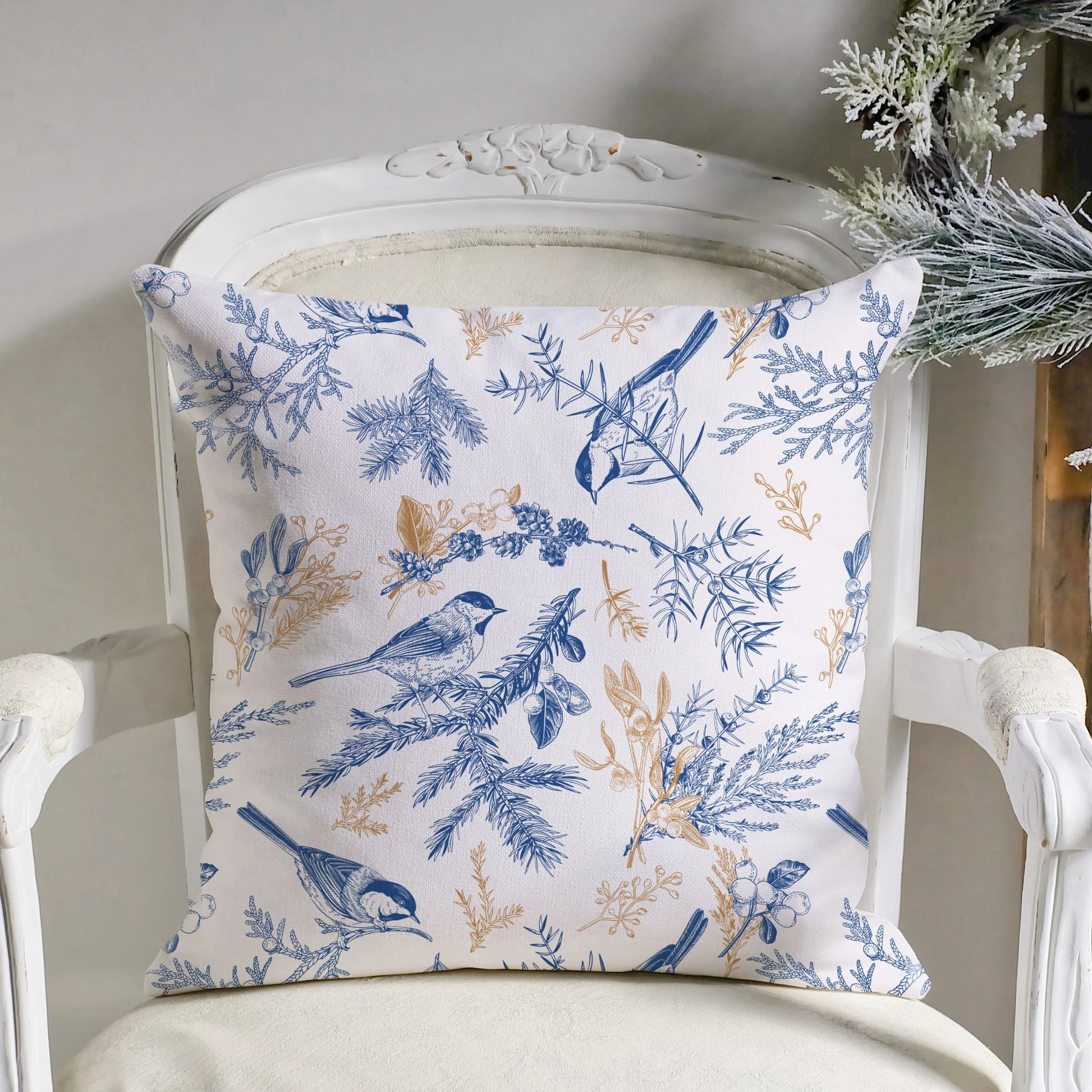 Vintage blue bird botanical winter pillow with gold botanicals on white chair with frosted greenery