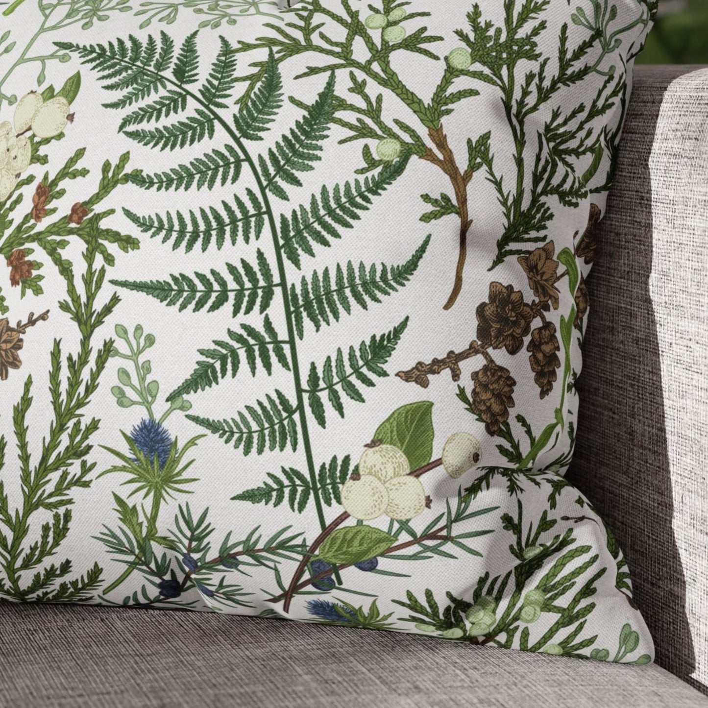 Close-up of vintage winter botanical pillow with green fern, pinecones, and berries on neutral sofa