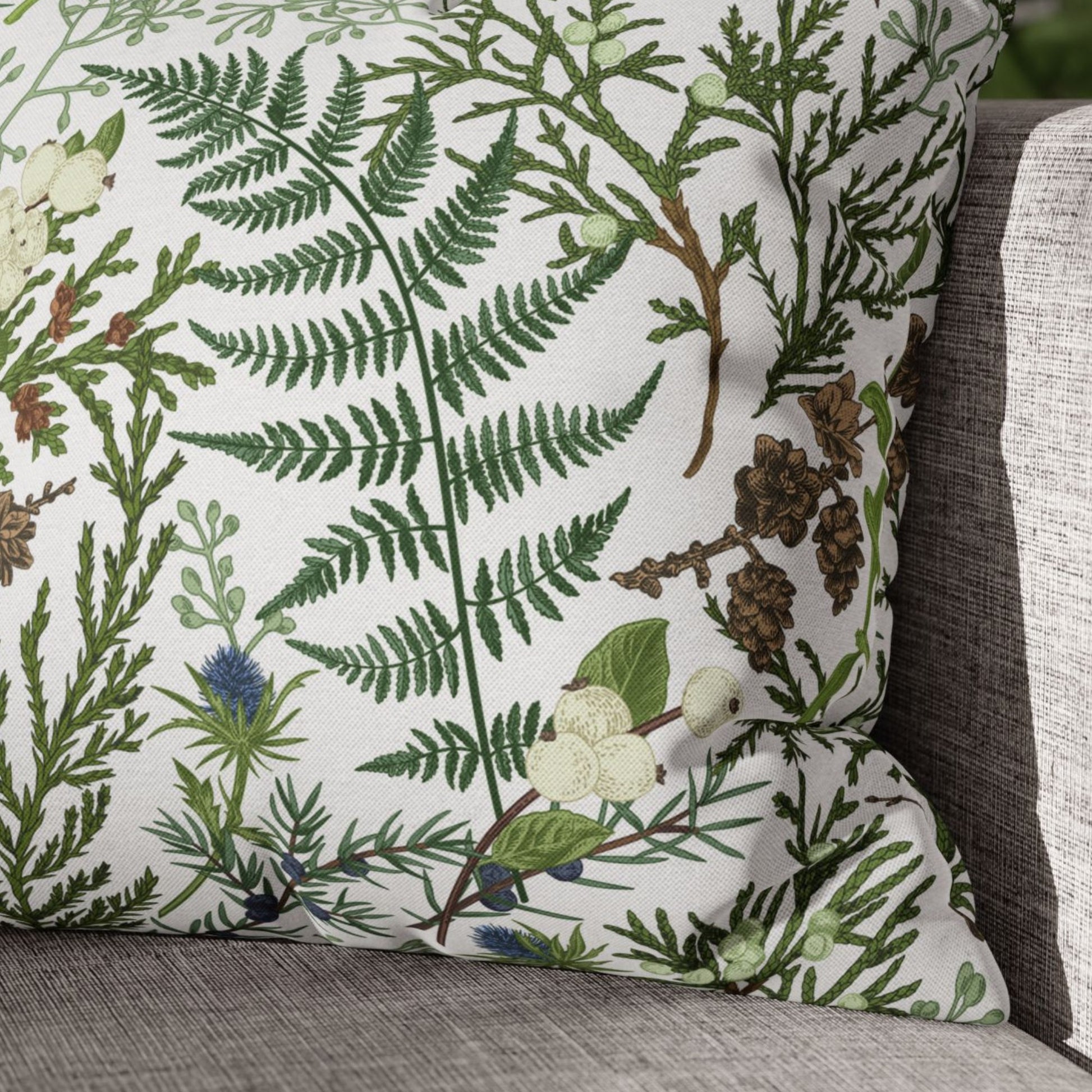 Close-up of vintage winter botanical pillow with green fern, pinecones, and berries on neutral sofa