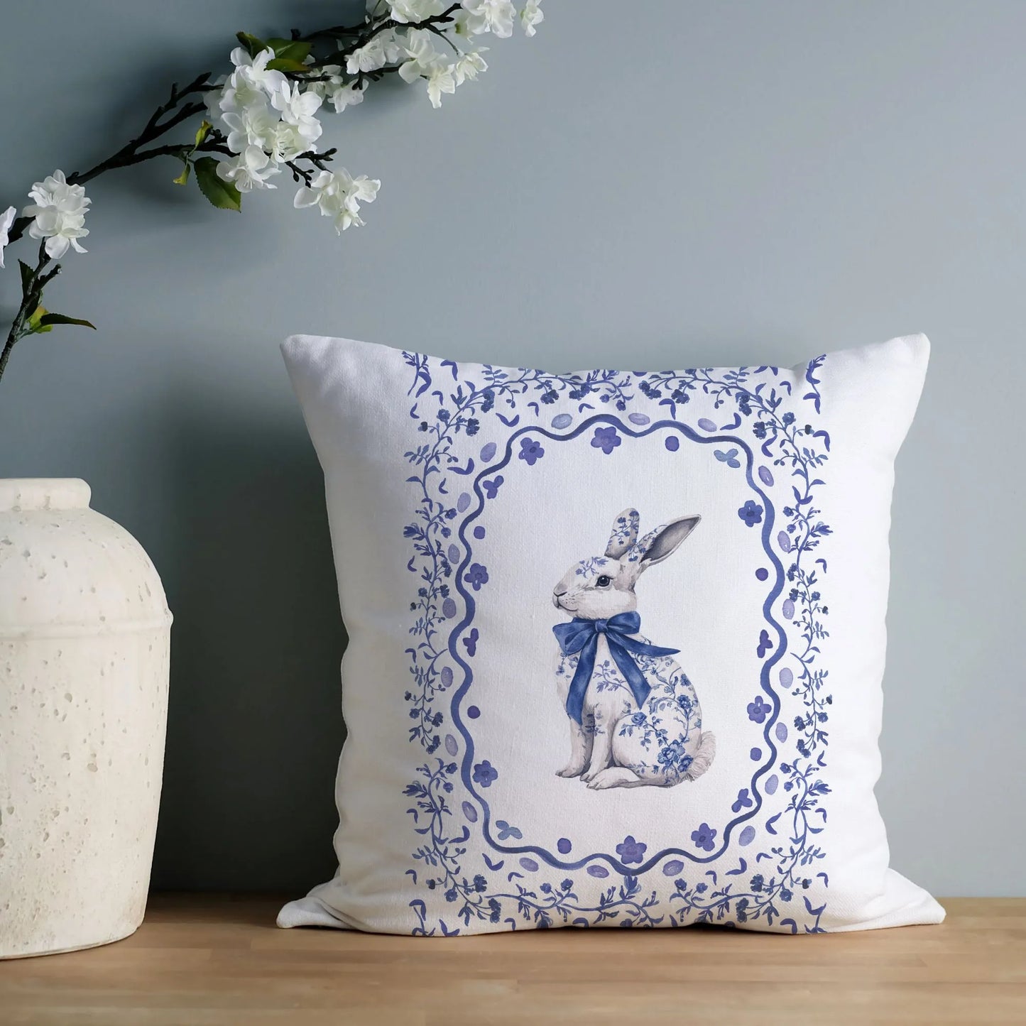 Blue watercolor Chinoiserie rabbit pillow with a floral frame, styled with white blossoms for elegant spring decor.