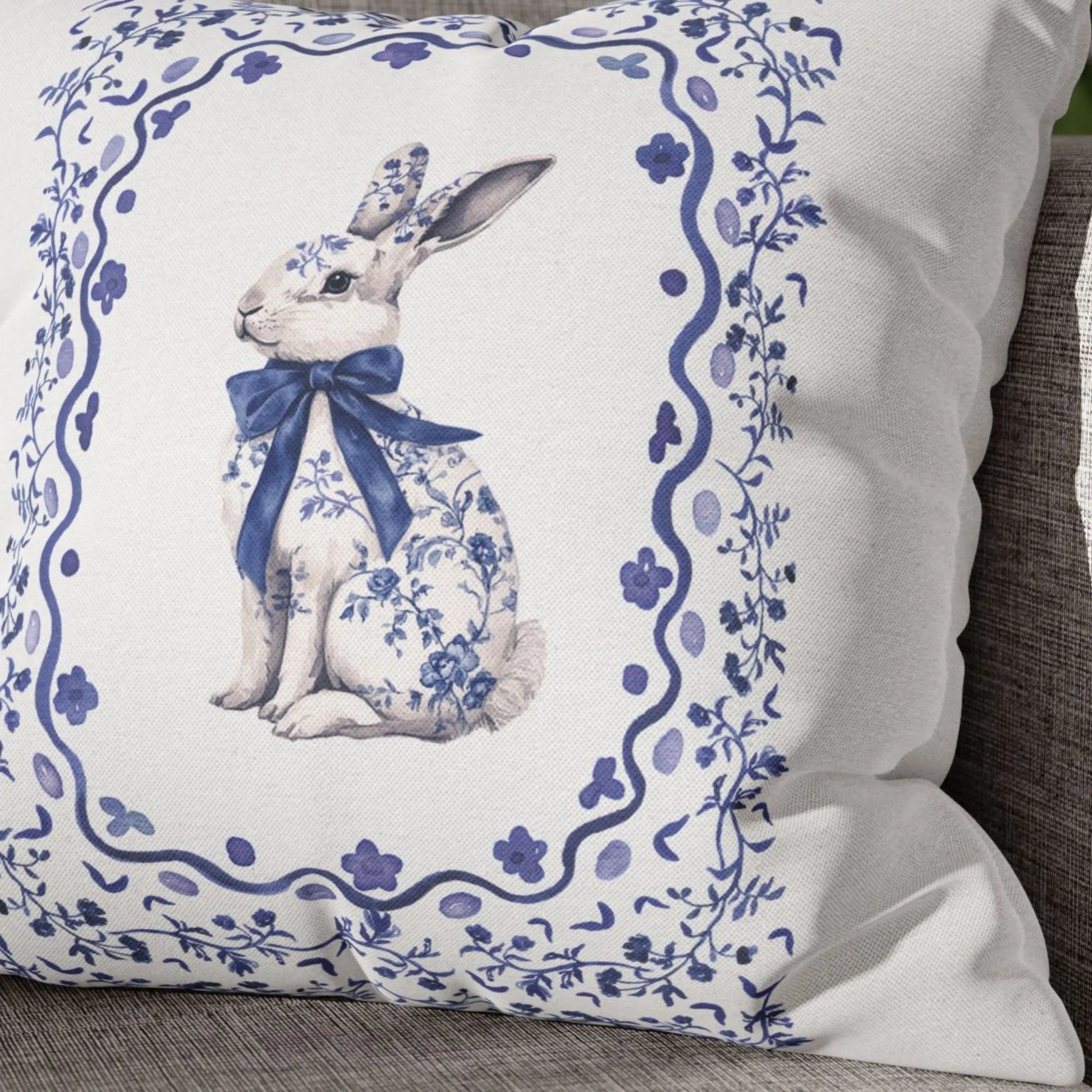 Close-up of a white pillow with a blue watercolor Chinoiserie rabbit wearing a bow and surrounded by a floral design.