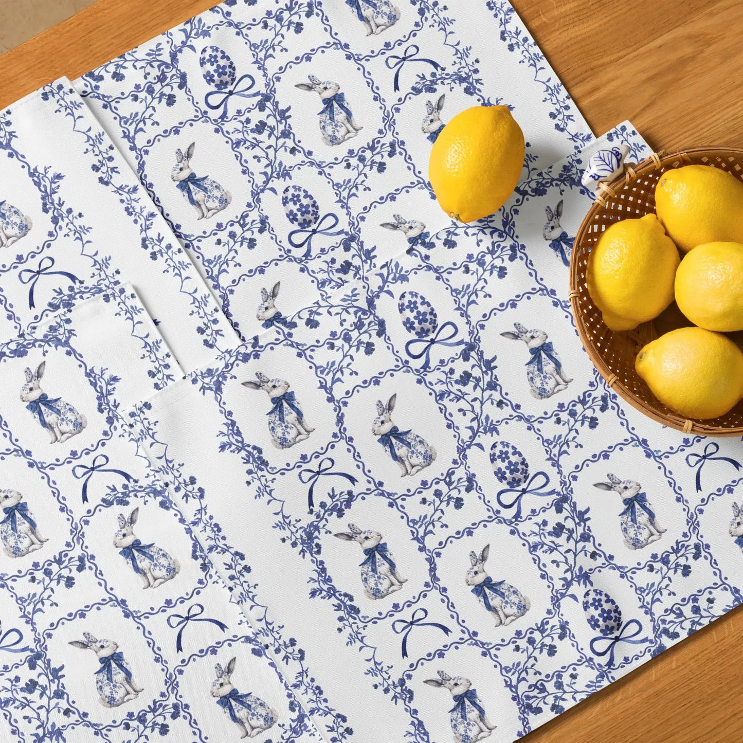 Blue and white placemats with a watercolor Chinoiserie rabbit and floral design on a light wood table with lemons.