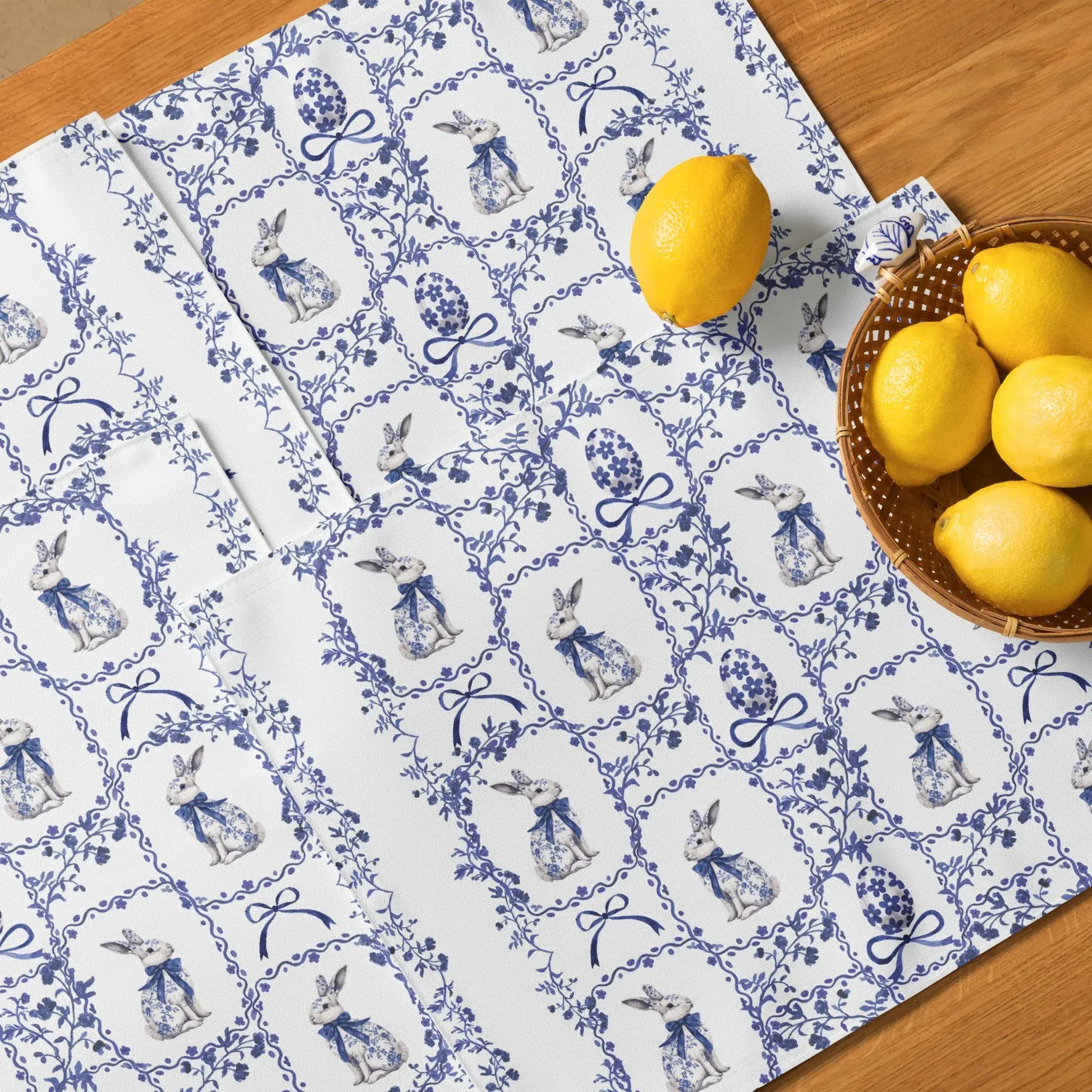 Blue and white placemats with a watercolor Chinoiserie rabbit and floral design on a light wood table with lemons.