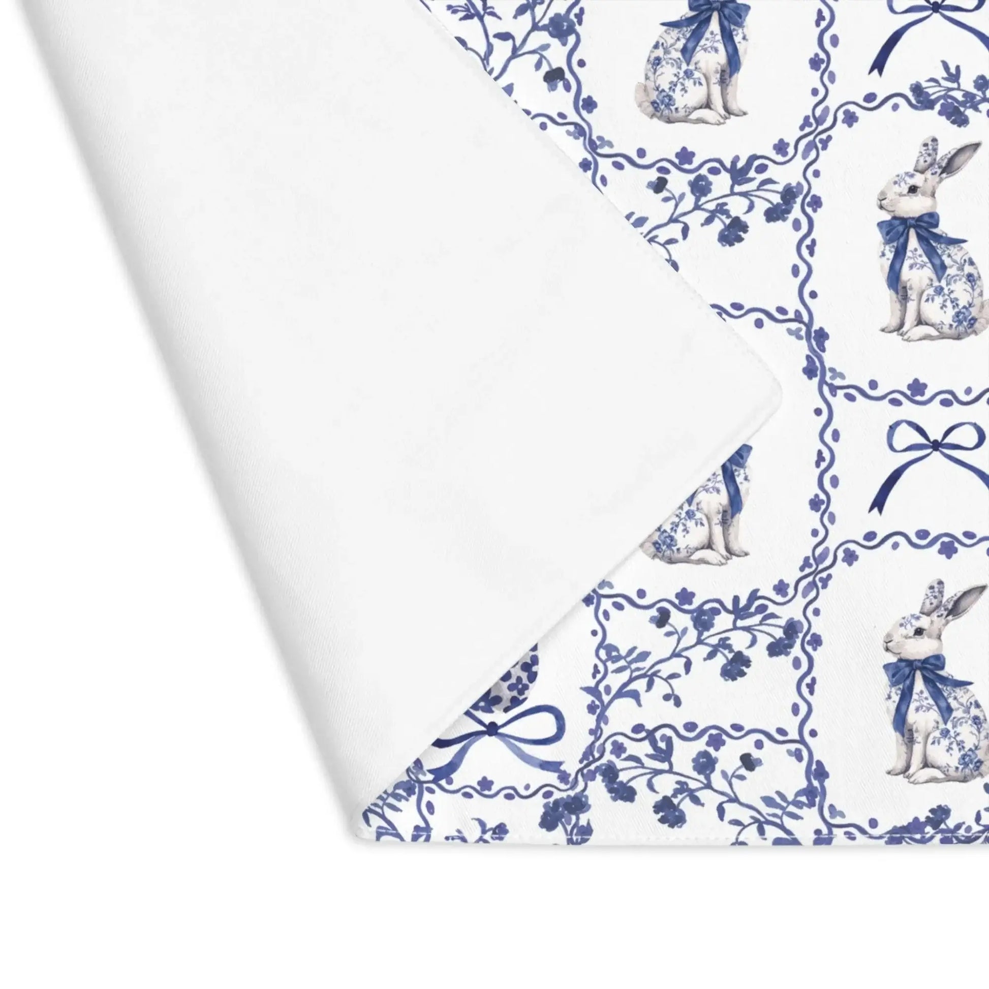 Close-up corner of a white cotton placemat showing the blue watercolor Chinoiserie rabbit, floral details, and fabric texture.