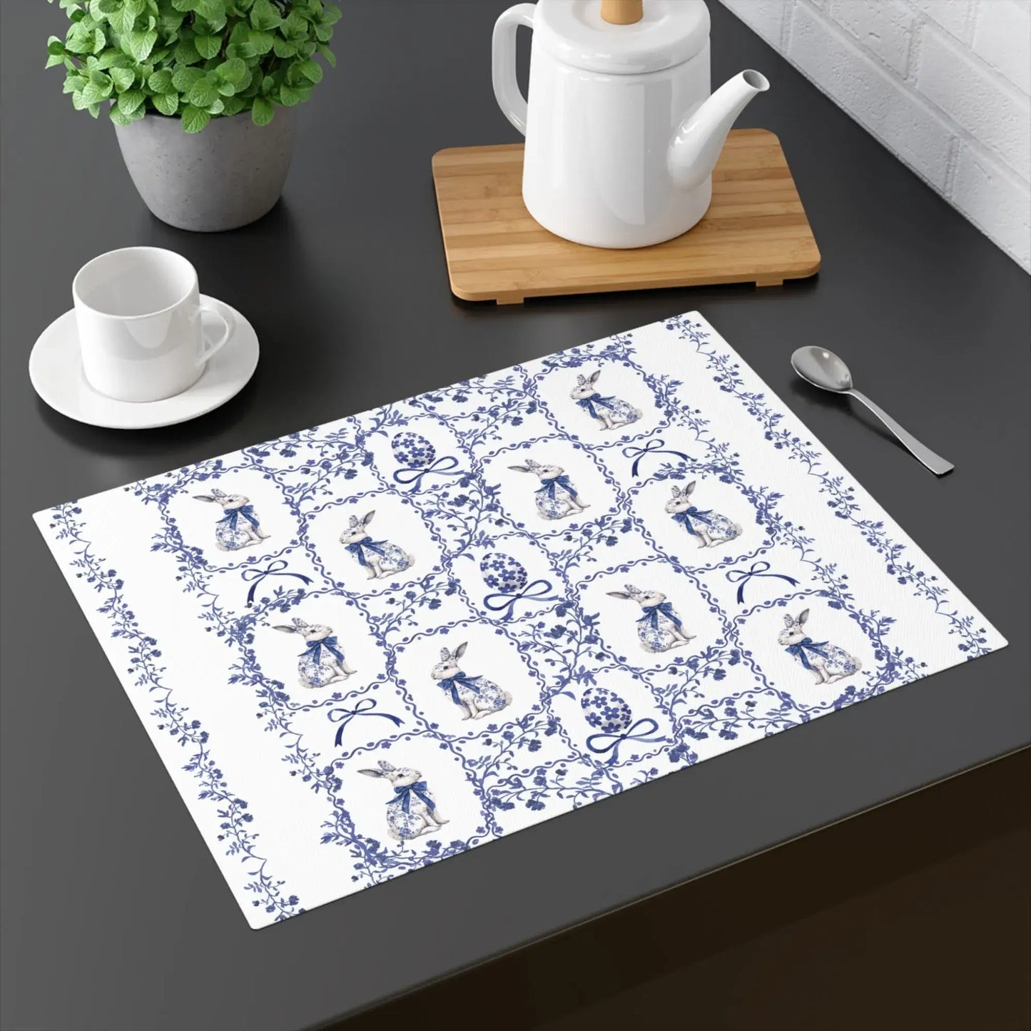 Blue and white placemat with a watercolor Chinoiserie rabbit and floral design on a dark table with a teacup and spoon.