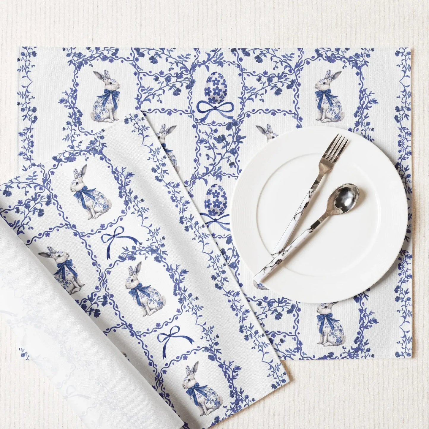 Blue and white placemat with a watercolor Chinoiserie rabbit, Easter egg, and floral design, set with a plate and silverware.