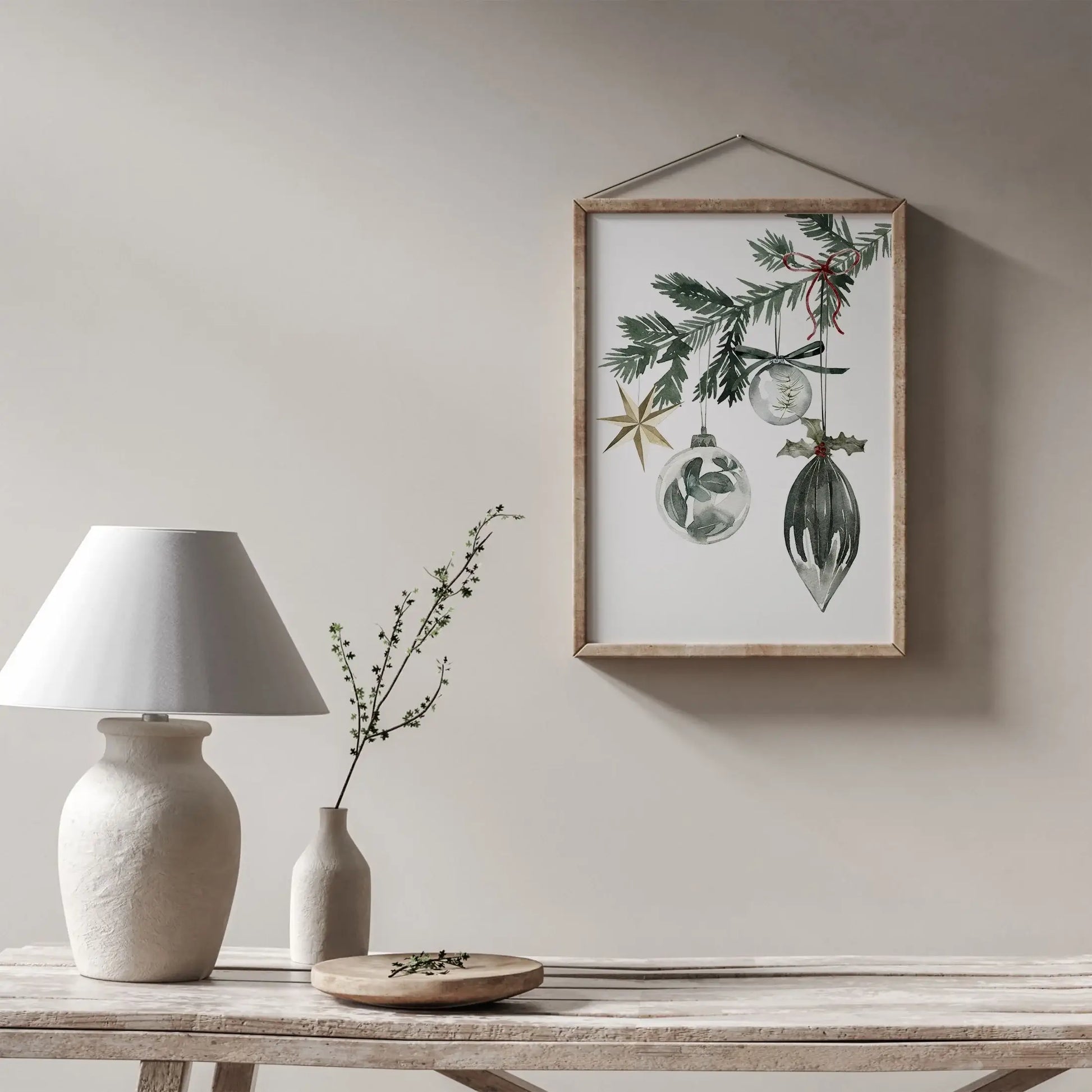 Christmas Ornaments Print Art featuring watercolor decorations hanging on a wall above a neutral-toned table and lamp.