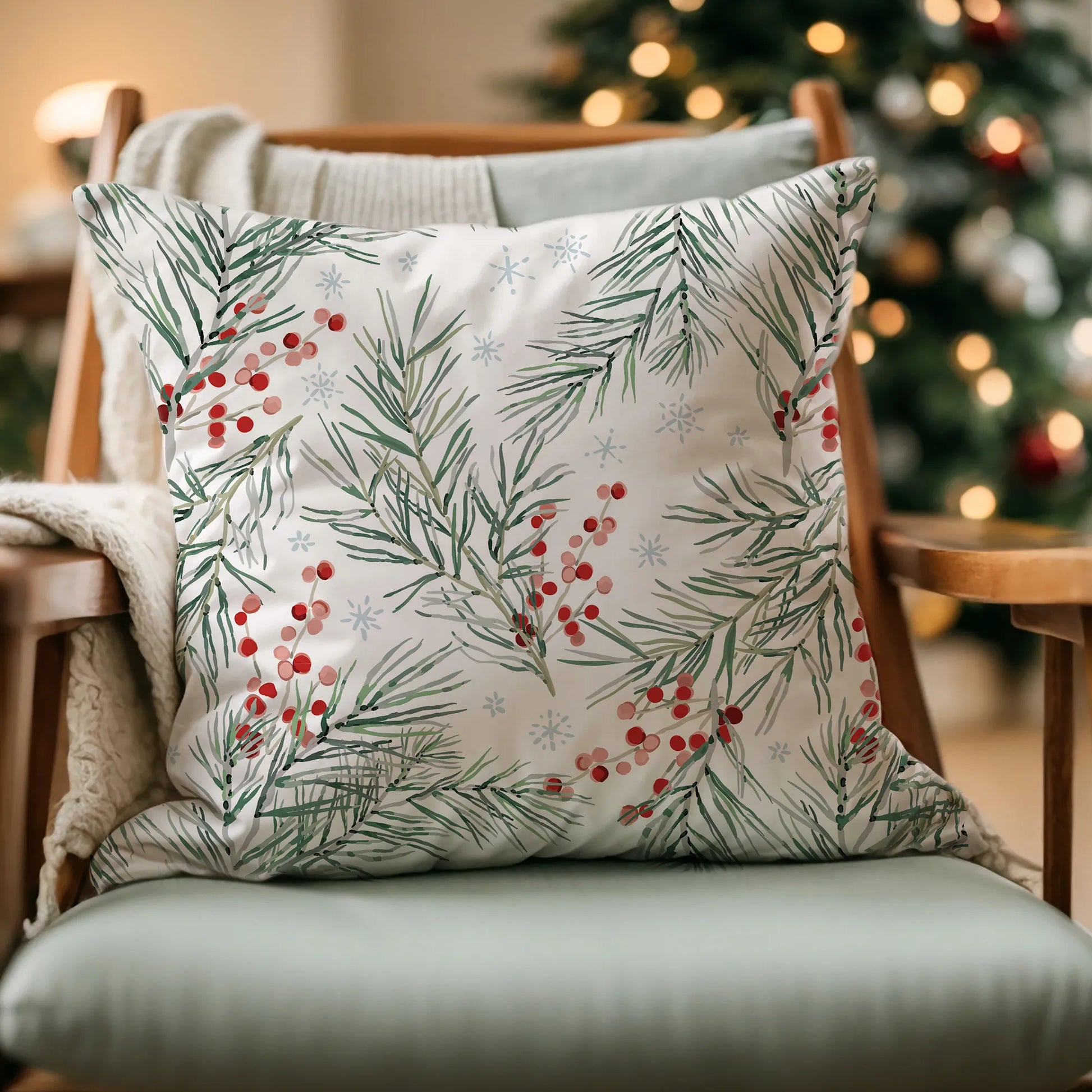 White pillow with watercolor pine branches and red berries on chair in front of Christmas tree