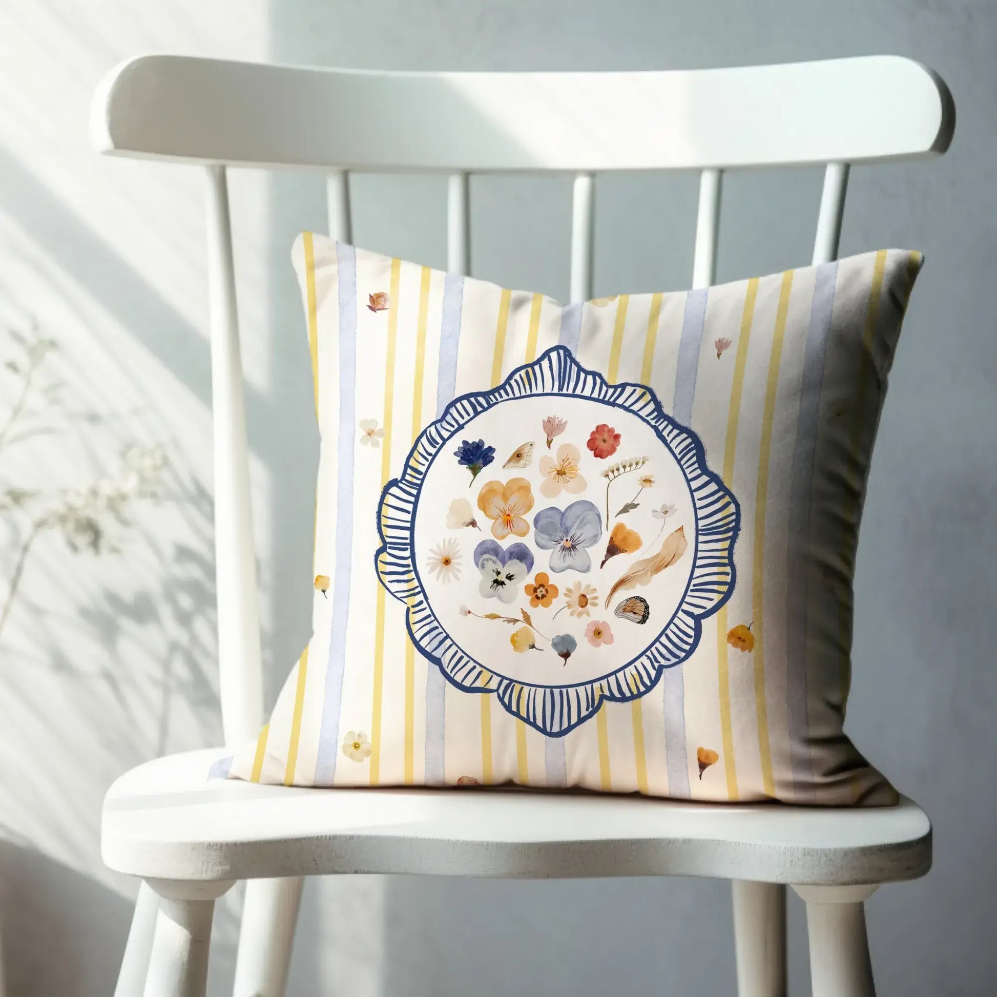 Watercolor Pressed Wildflower Pillow with floral design on striped background sitting on a wooden chair.