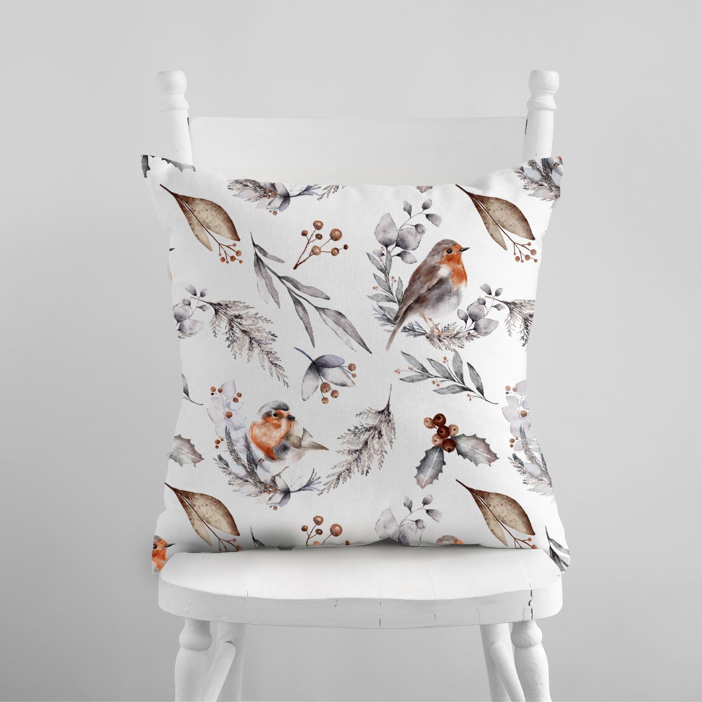White pillow with watercolor robins and winter botanicals – soft seasonal nature-inspired cushion on white chair
