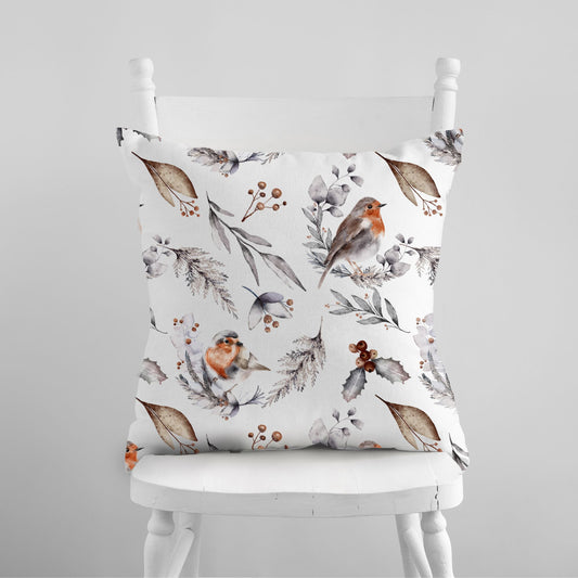 White pillow with watercolor robins and winter botanicals – soft seasonal nature-inspired cushion on white chair
