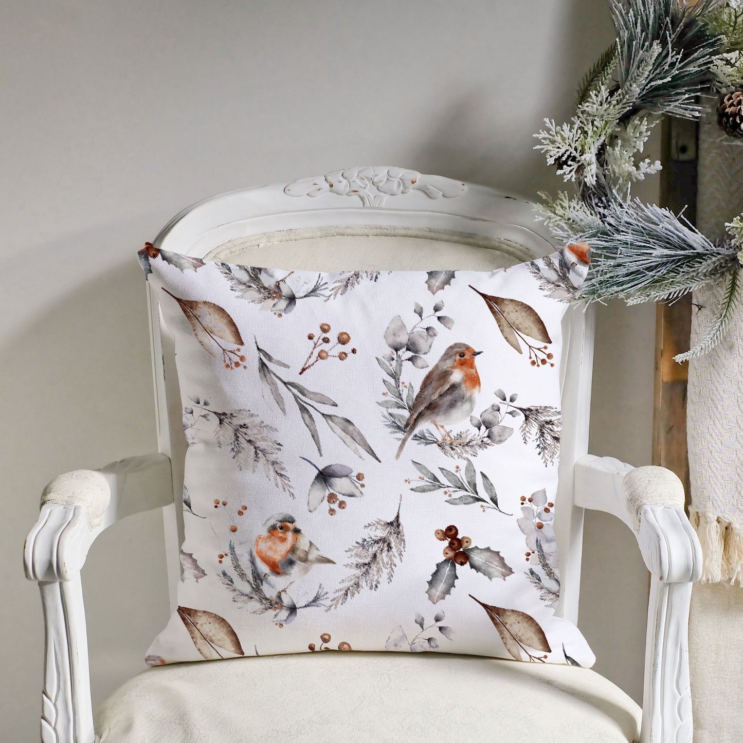 Watercolor robin pillow with winter foliage on vintage chair – soft Christmas cushion with frosted greenery nearby