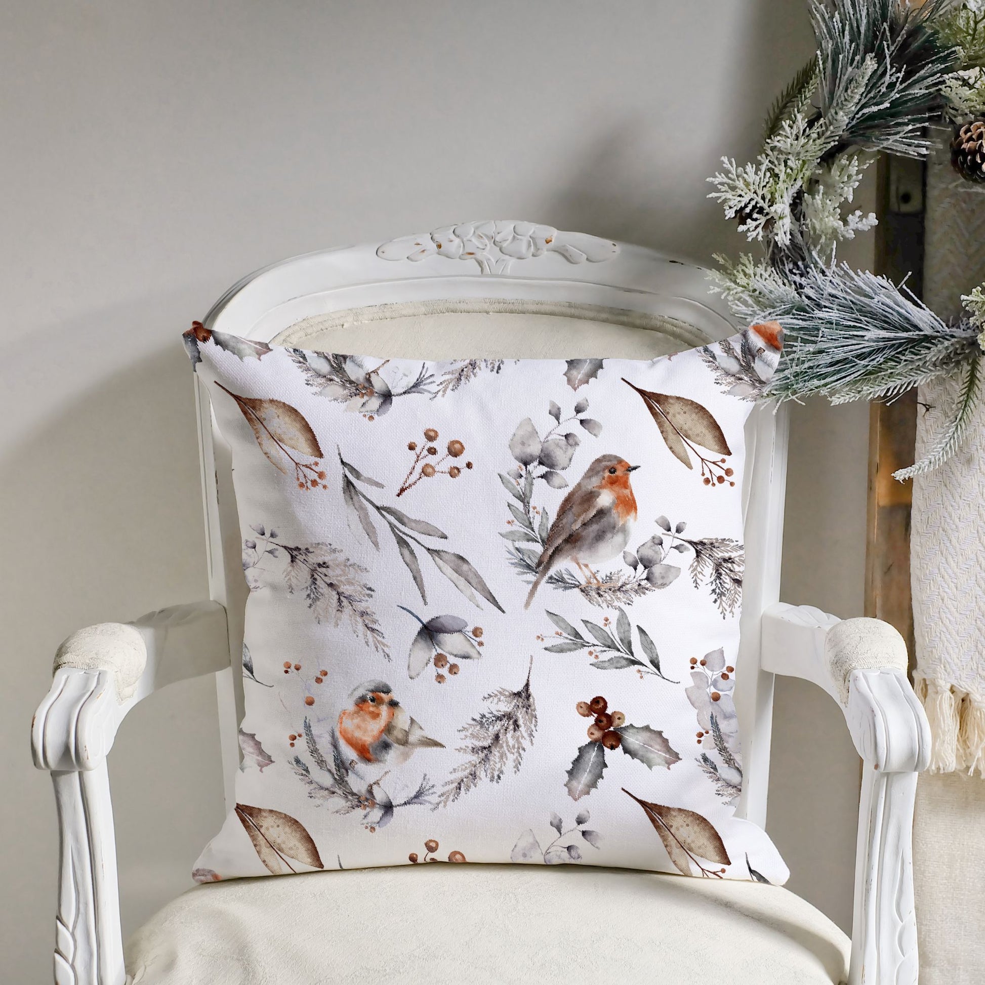 Watercolor robin pillow with winter foliage on vintage chair – soft Christmas cushion with frosted greenery nearby