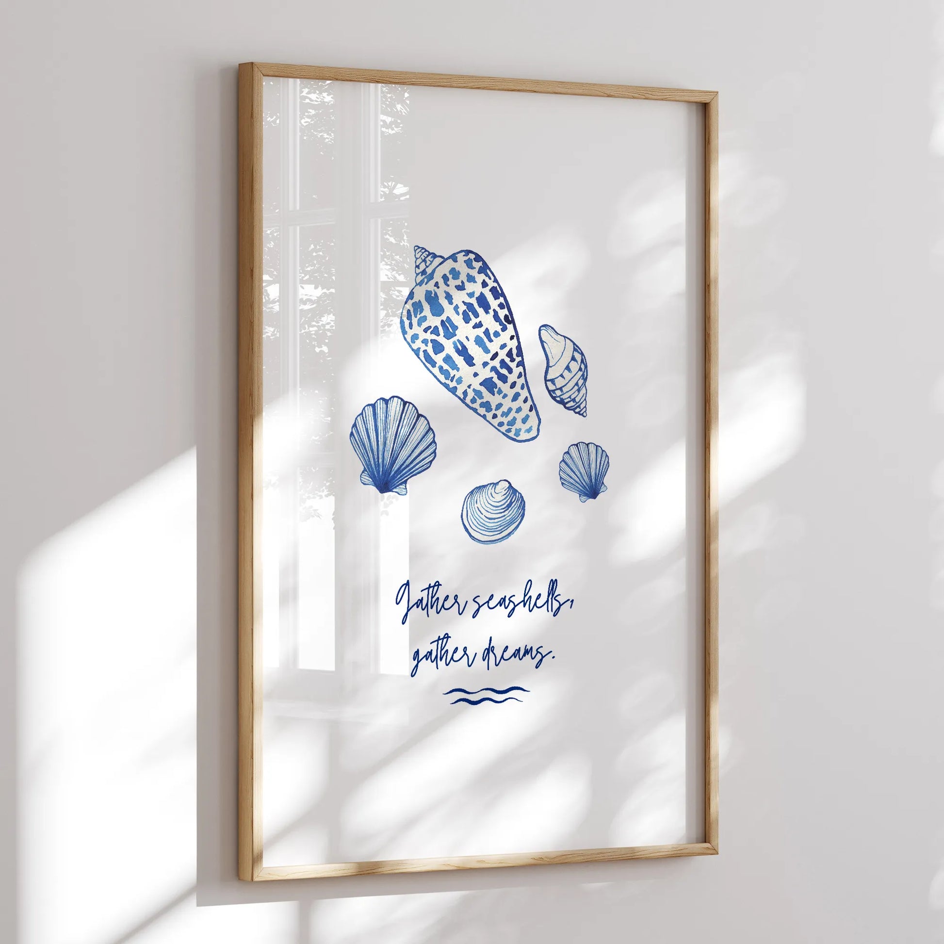 Framed watercolor seashell art print with coastal blue seashells and "Gather seashells, gather dreams" quote, displayed in natural sunlight.