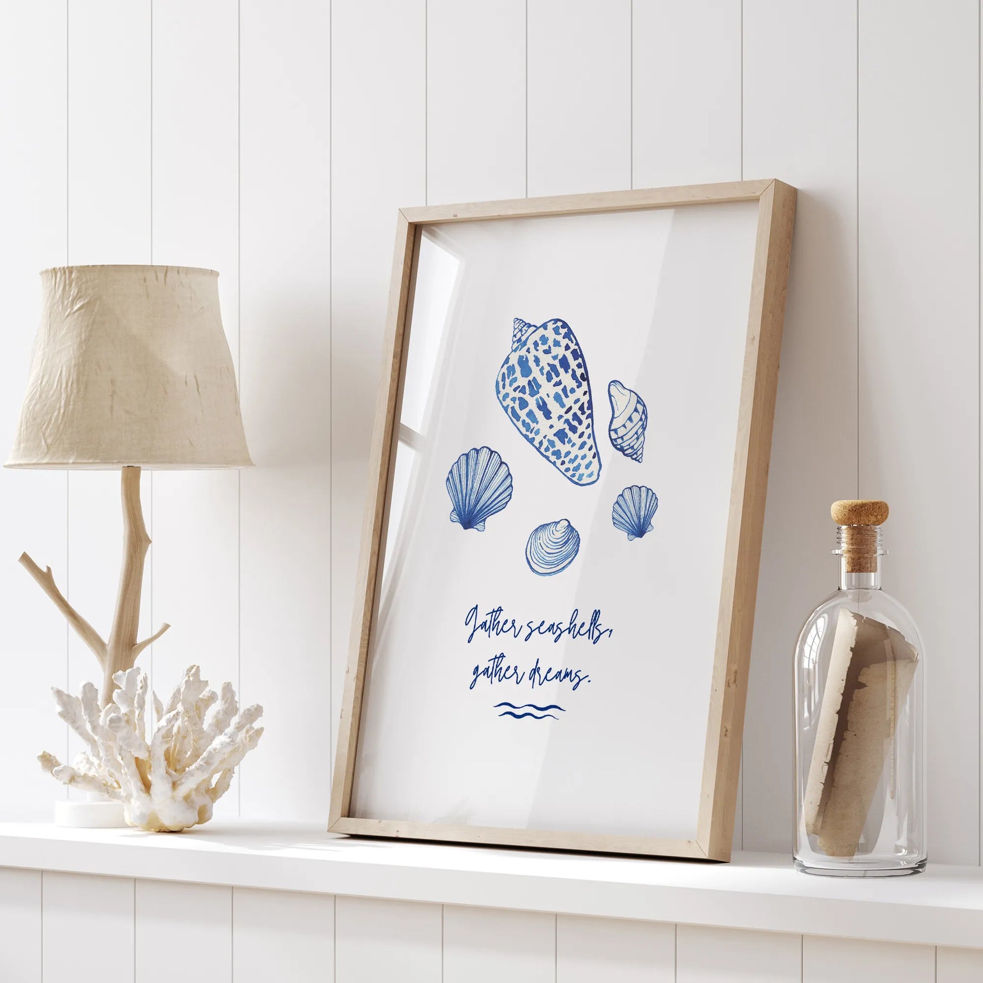 Coastal watercolor seashells art print displayed on white shelf with nautical decor, featuring "Gather seashells, gather dreams" quote.