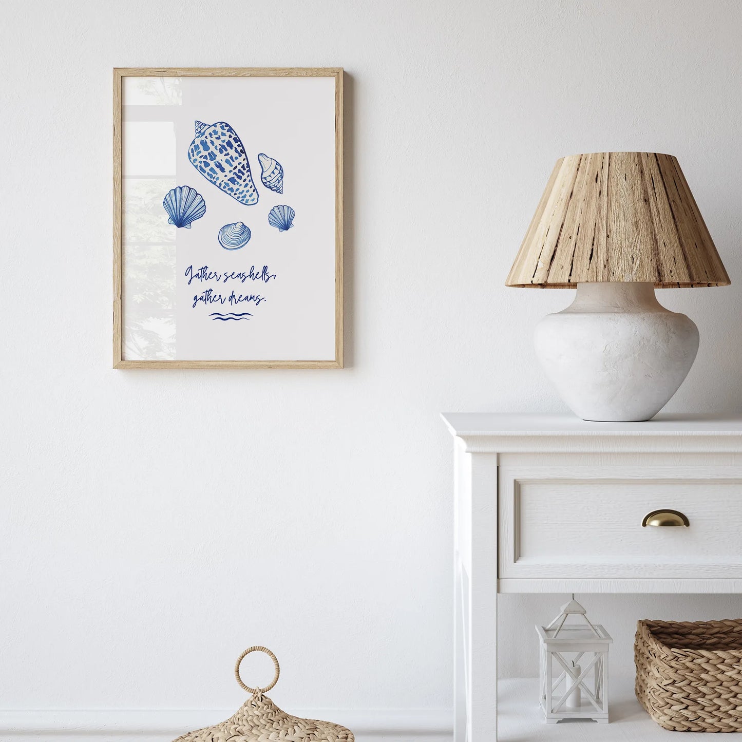 Coastal watercolor seashell art print displayed in a natural wood frame, styled on a white wall with a woven lamp and basket decor.