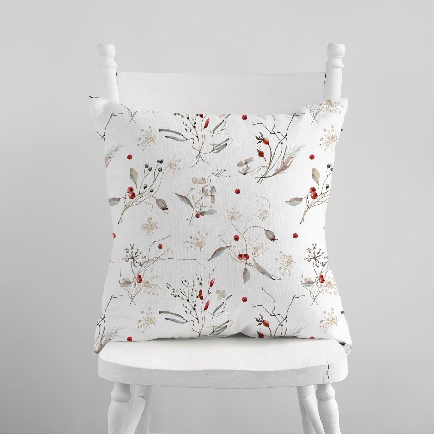 Watercolor winter botanical pillow with red berries on white chair – nature-inspired seasonal decor
