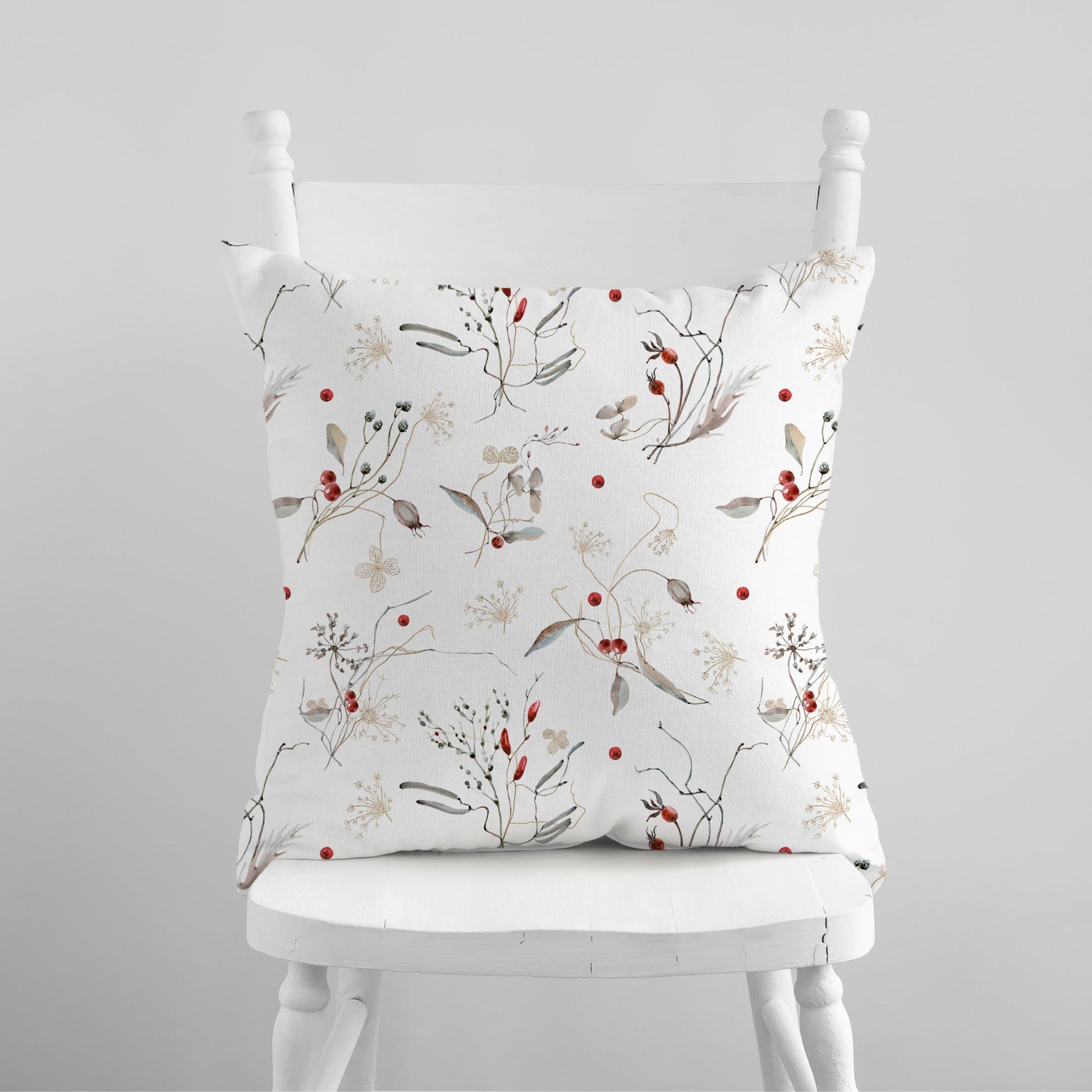 Watercolor winter botanical pillow with red berries on white chair – nature-inspired seasonal decor