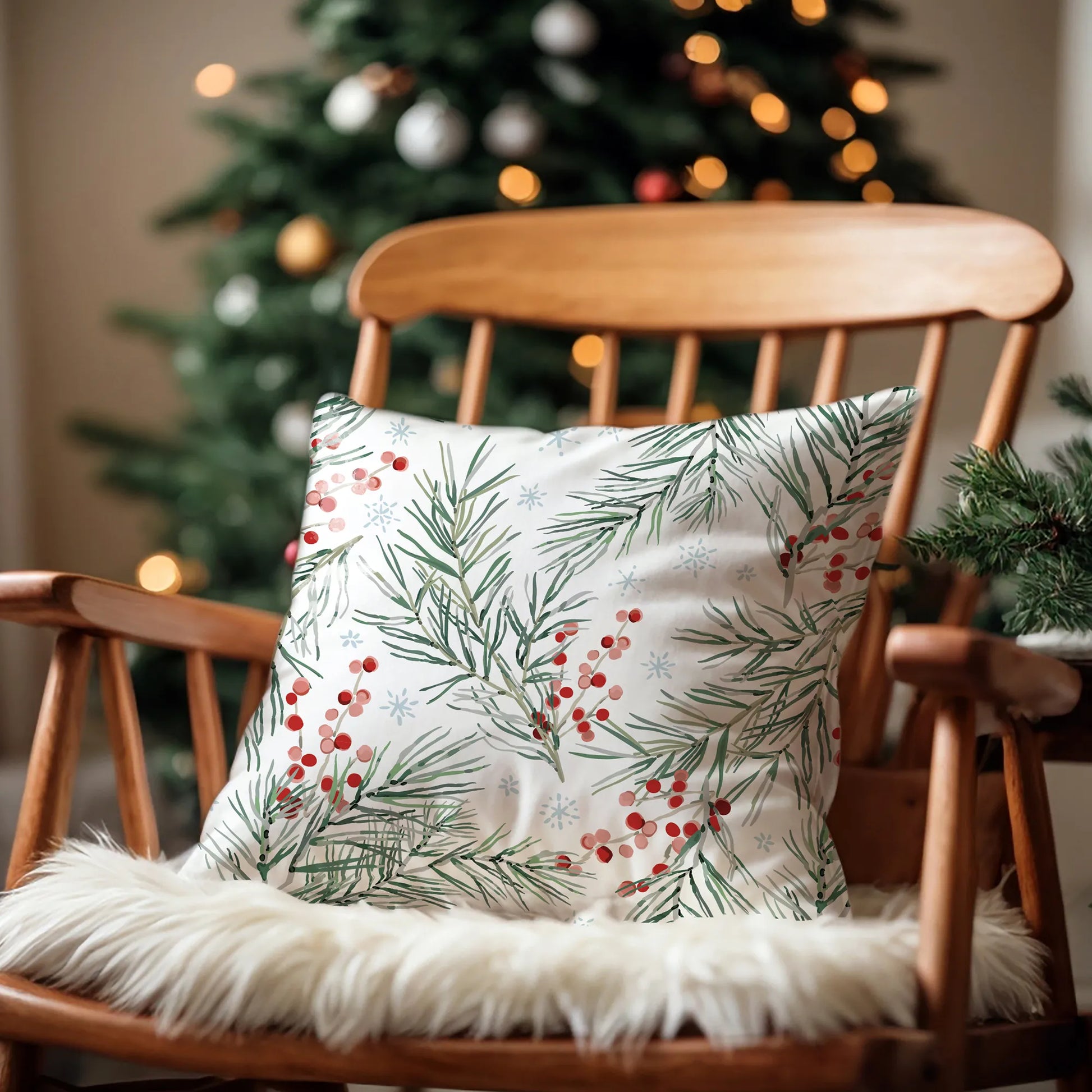 White Christmas pillow with pine branches and red berries on chair by holiday tree