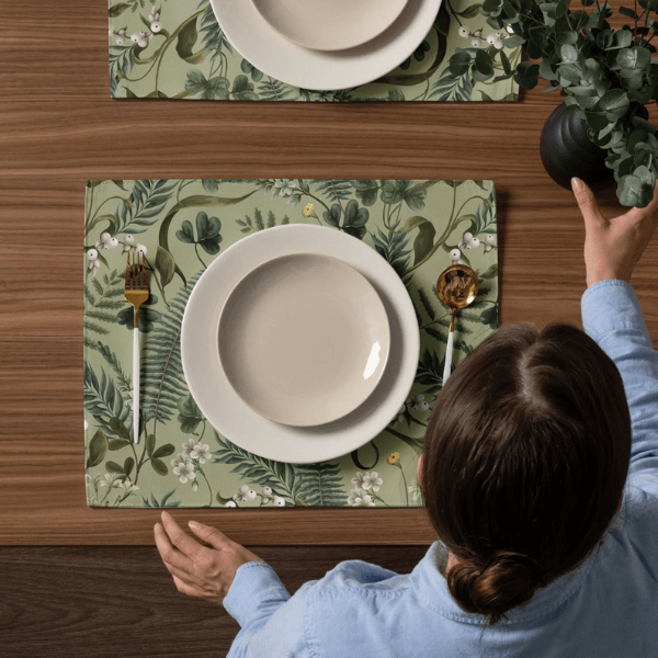 Setting a table with Wild Fern Garden Placemats featuring botanical designs and a white plate on a wooden table.