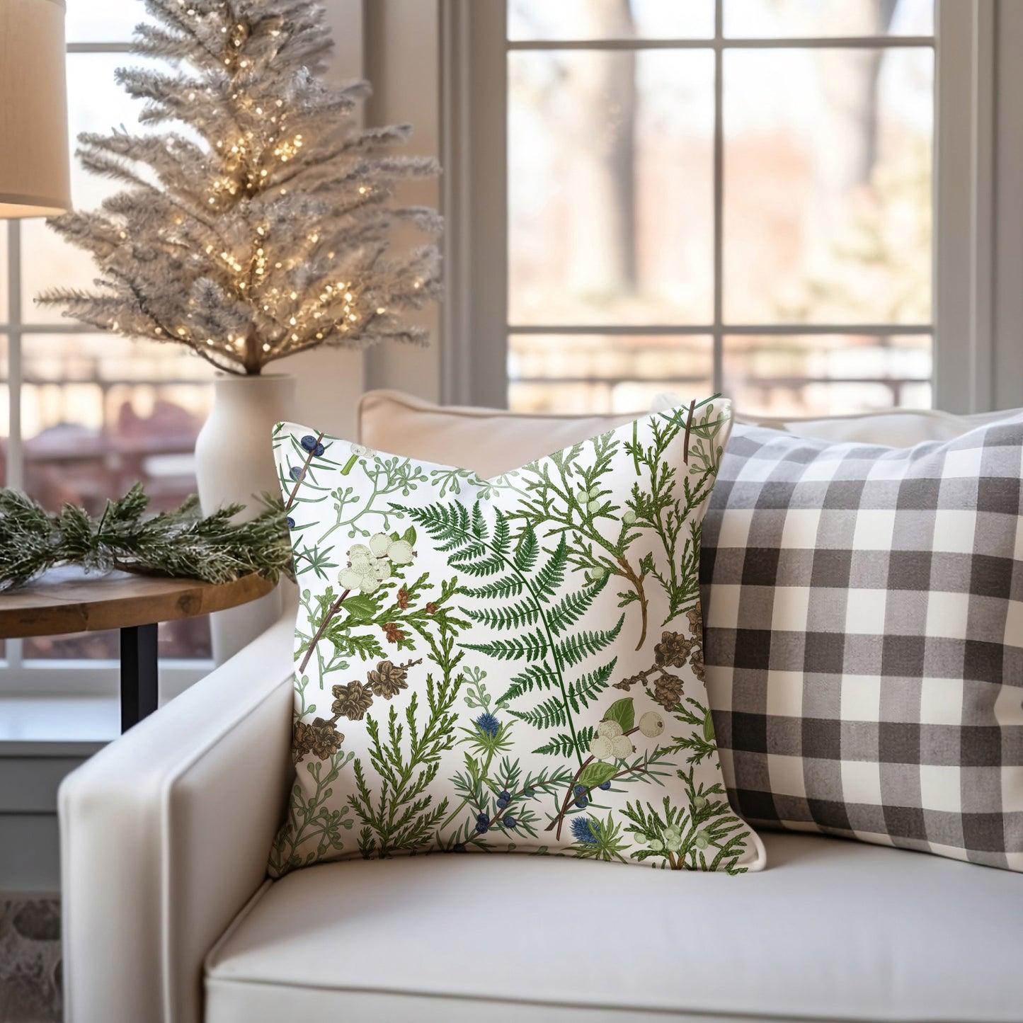Winter botanical pillow with fern and pinecones on white sofa – cozy seasonal decor with Christmas tree