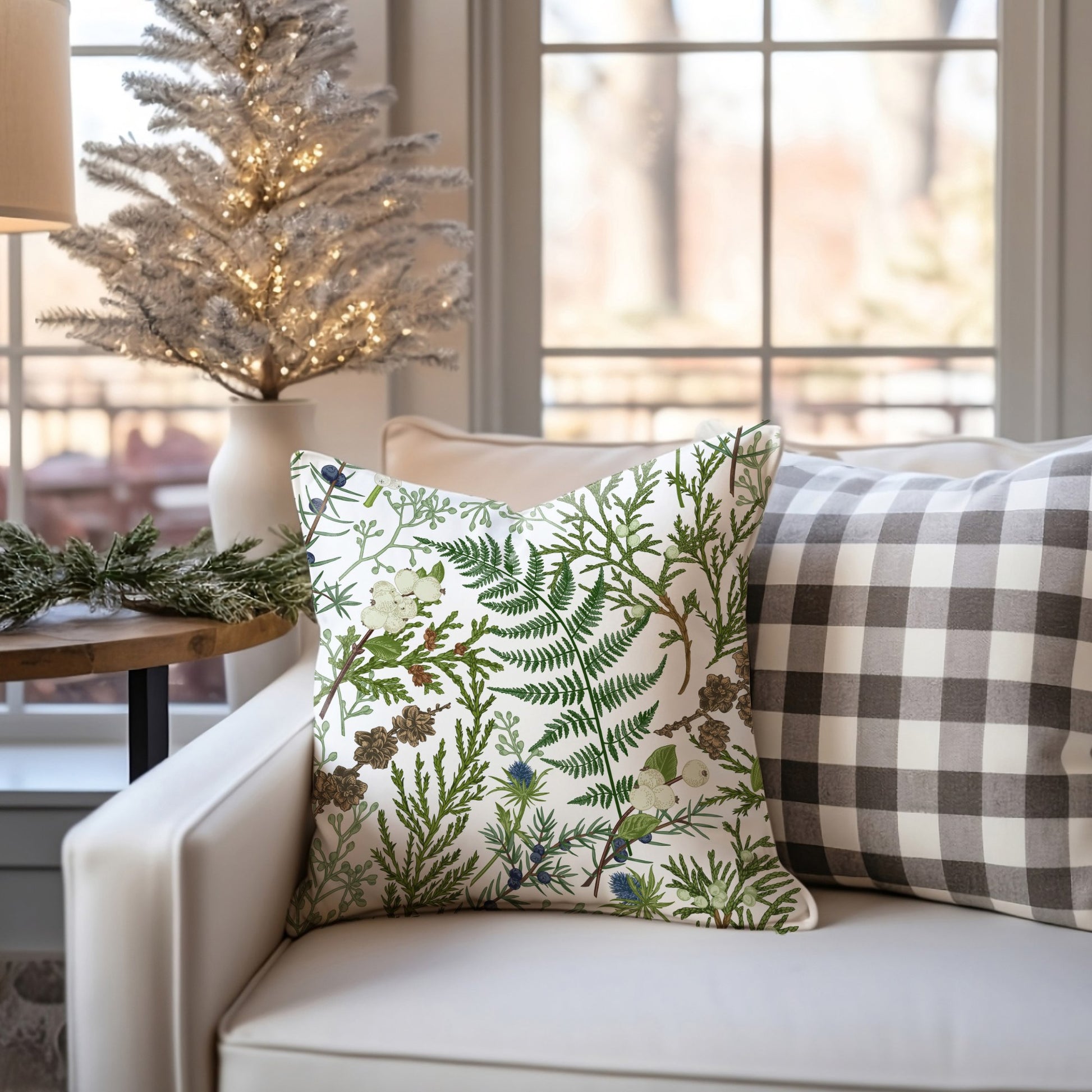 Winter botanical pillow with fern and pinecones on white sofa – cozy seasonal decor with Christmas tree
