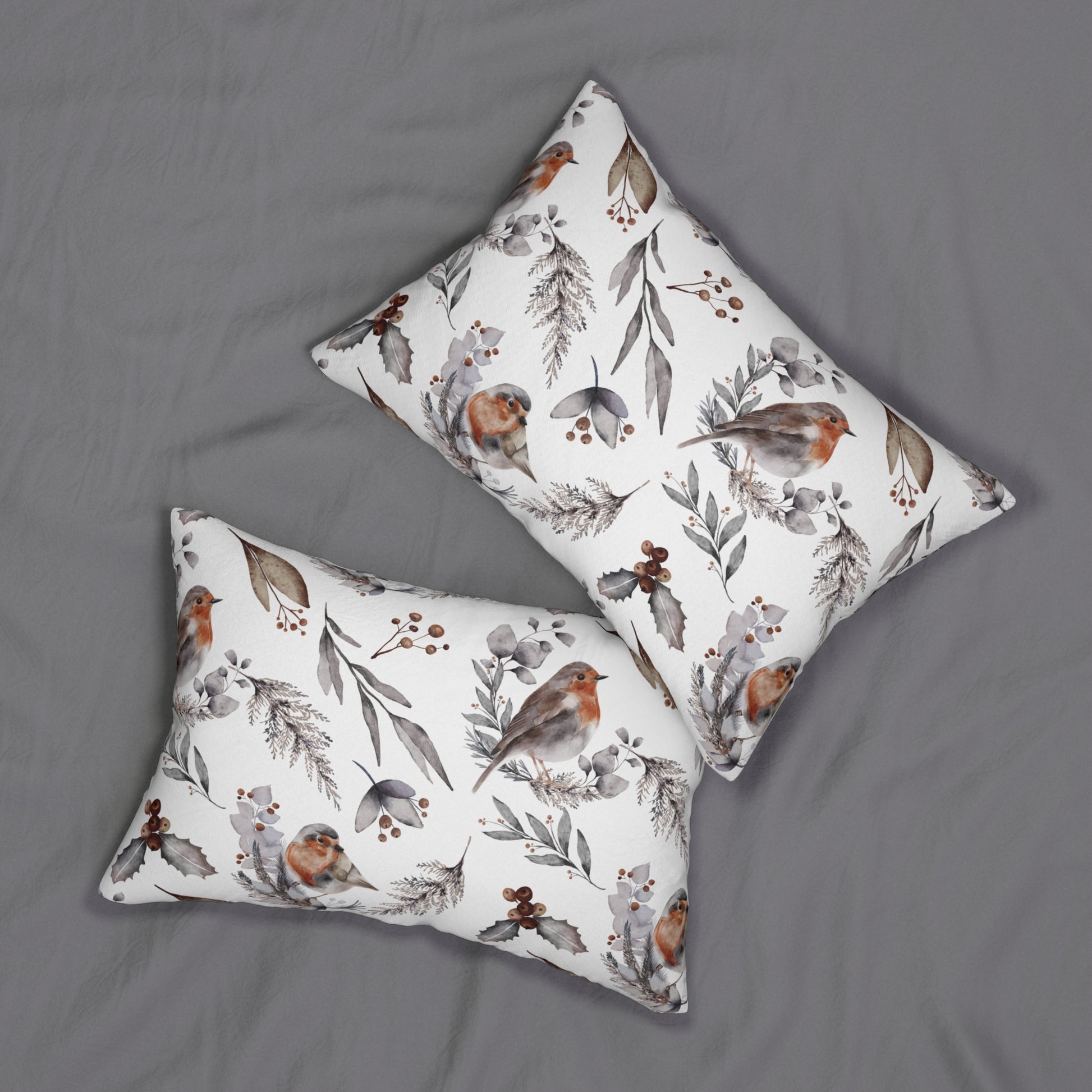 Two rectangular winter bird pillows with watercolor robin and botanical design on grey bed