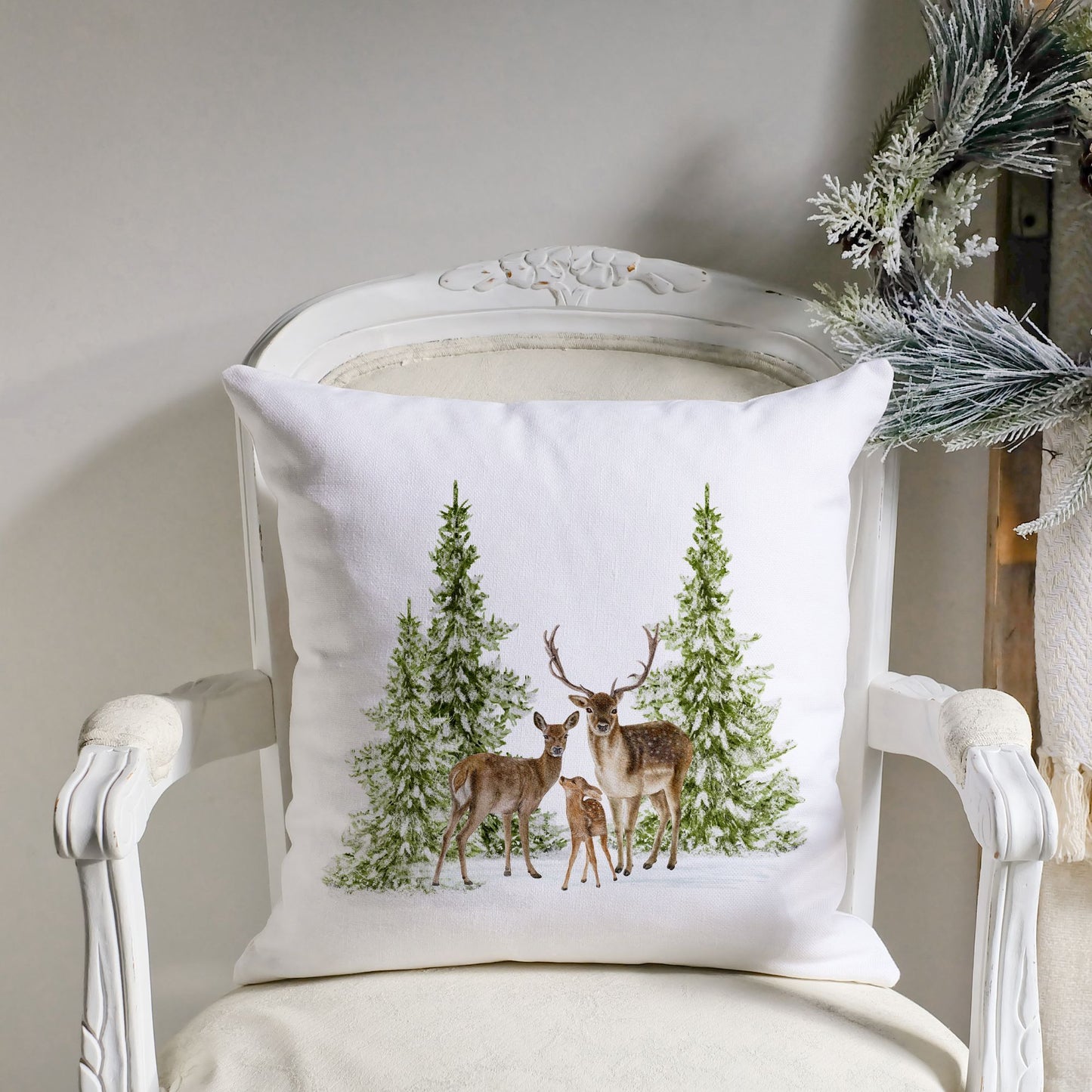 White Christmas pillow with deer and pine trees on vintage chair – cozy holiday decor