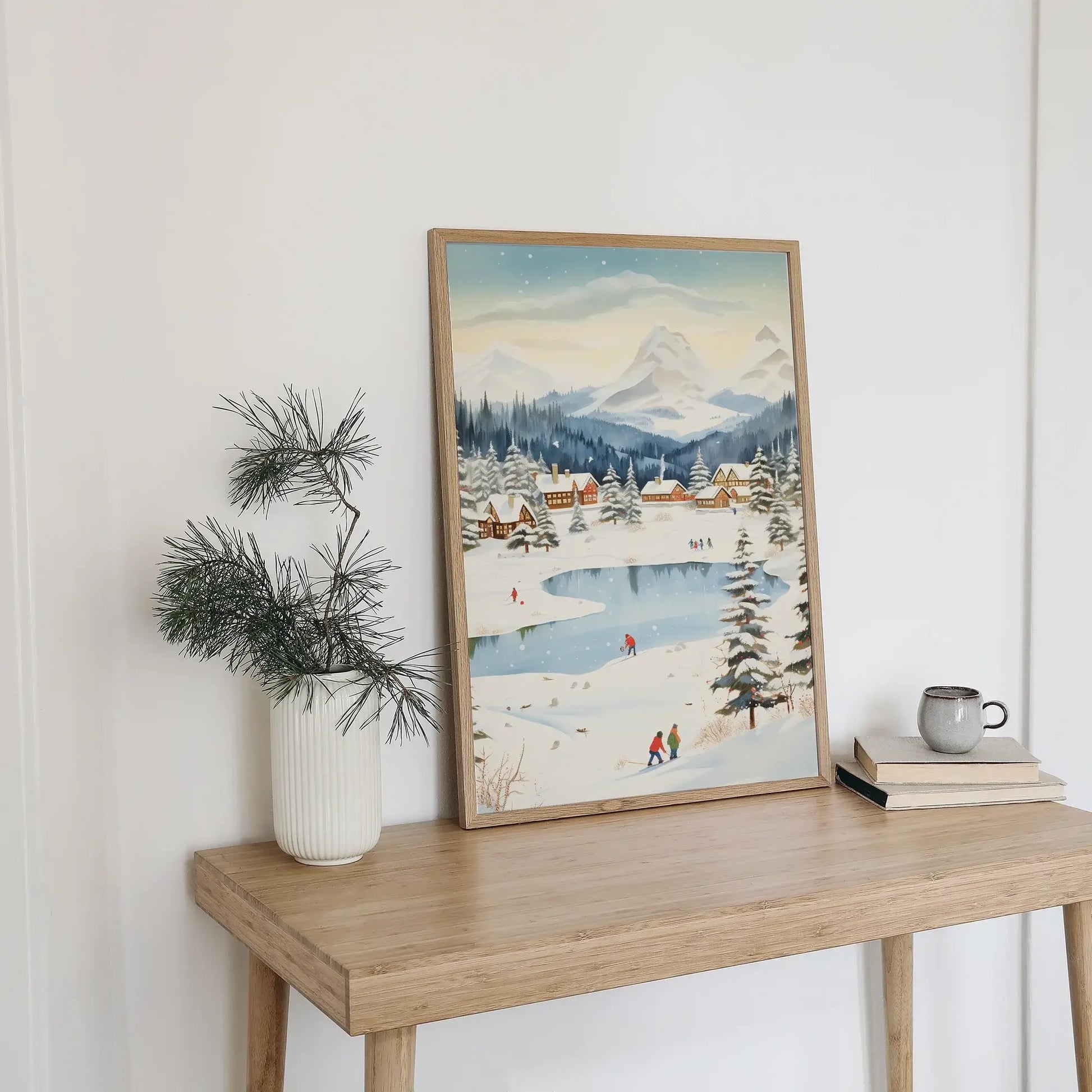 Winter Village Christmas Art Print displayed on a wooden table with a plant and mug.