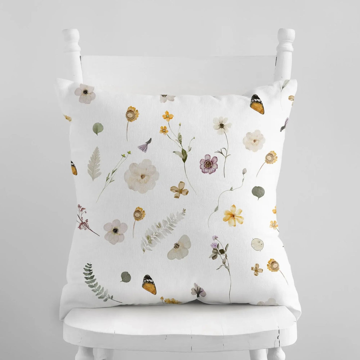 Yellow Watercolor Pressed Flowers PILLOW on a white chair with delicate floral designs.