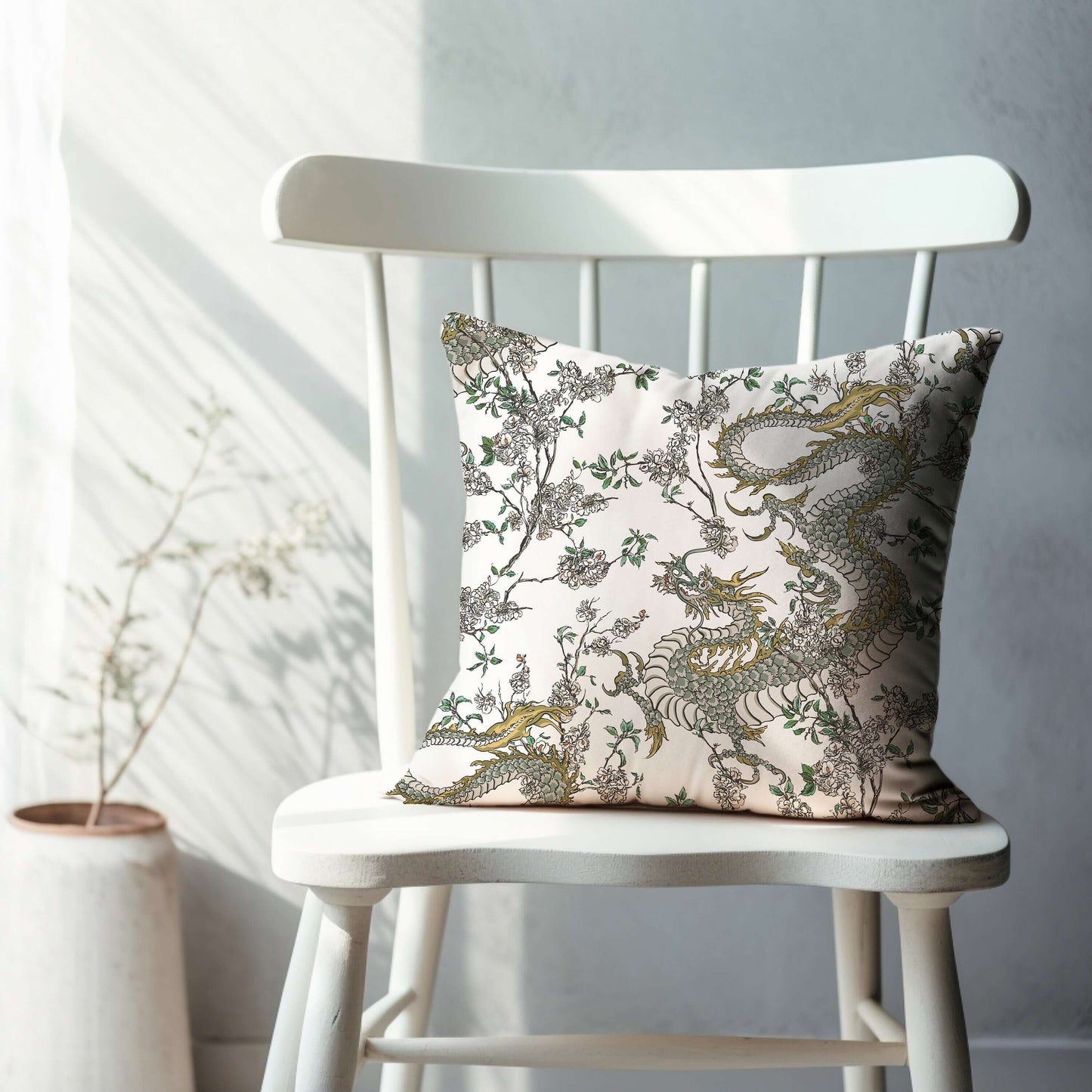 White chinoiserie pillow with dragon and floral design. Oriental decorative throw pillow on white chair.