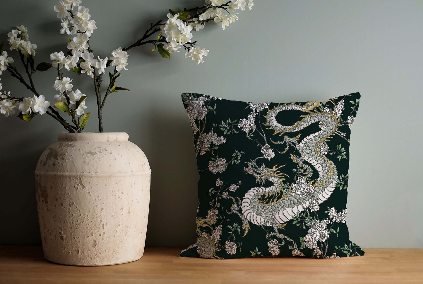 Dragon chinoiserie pillow on wooden surface. Dark green decorative pillow with oriental design and flowers.