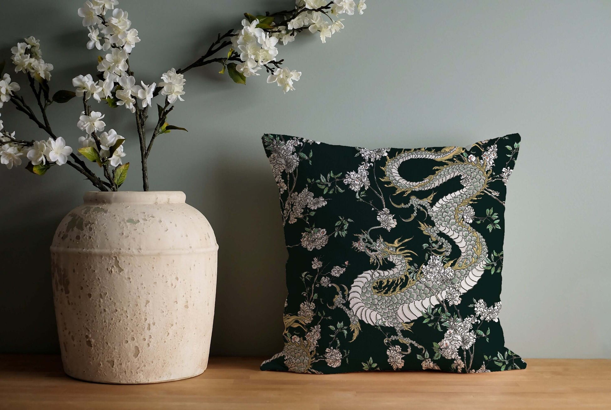 Dragon chinoiserie pillow on wooden surface. Dark green decorative pillow with oriental design and flowers.